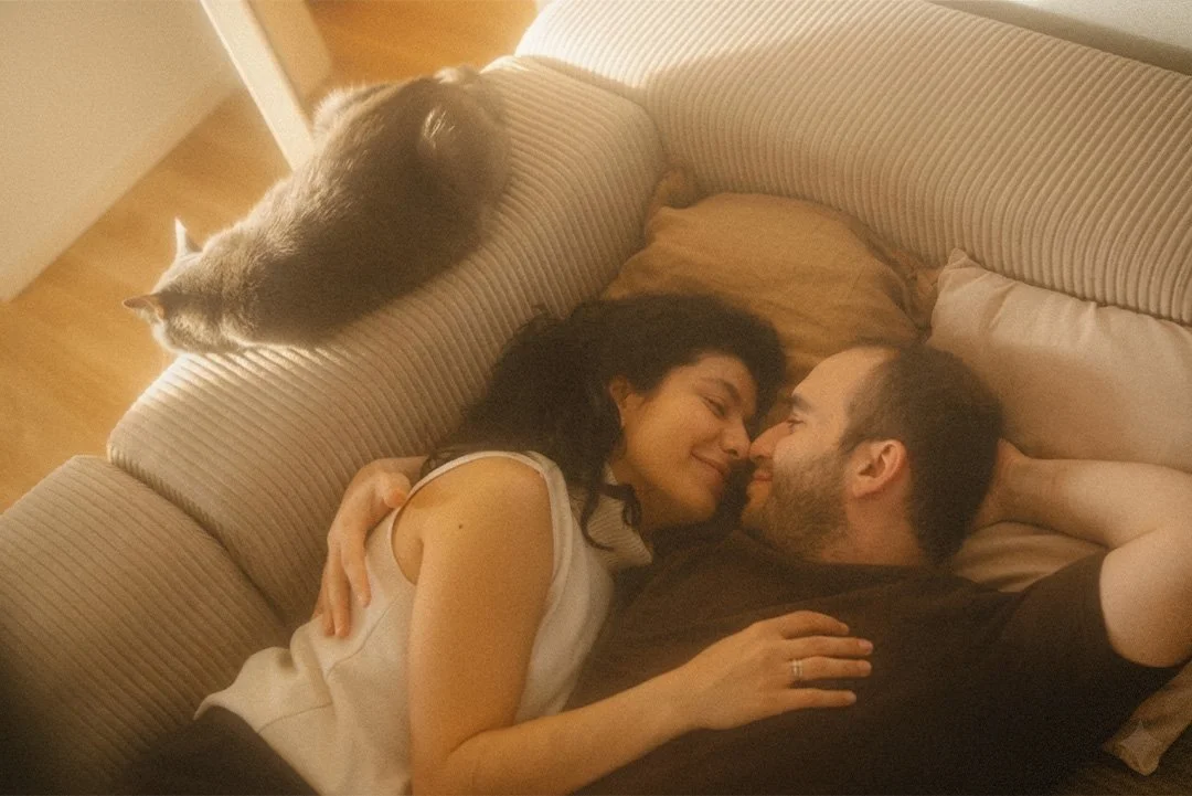 Overhead lifestyle portrait of a couple lying on a couch with their grey cat in a Berlin Kreuzberg apartment.