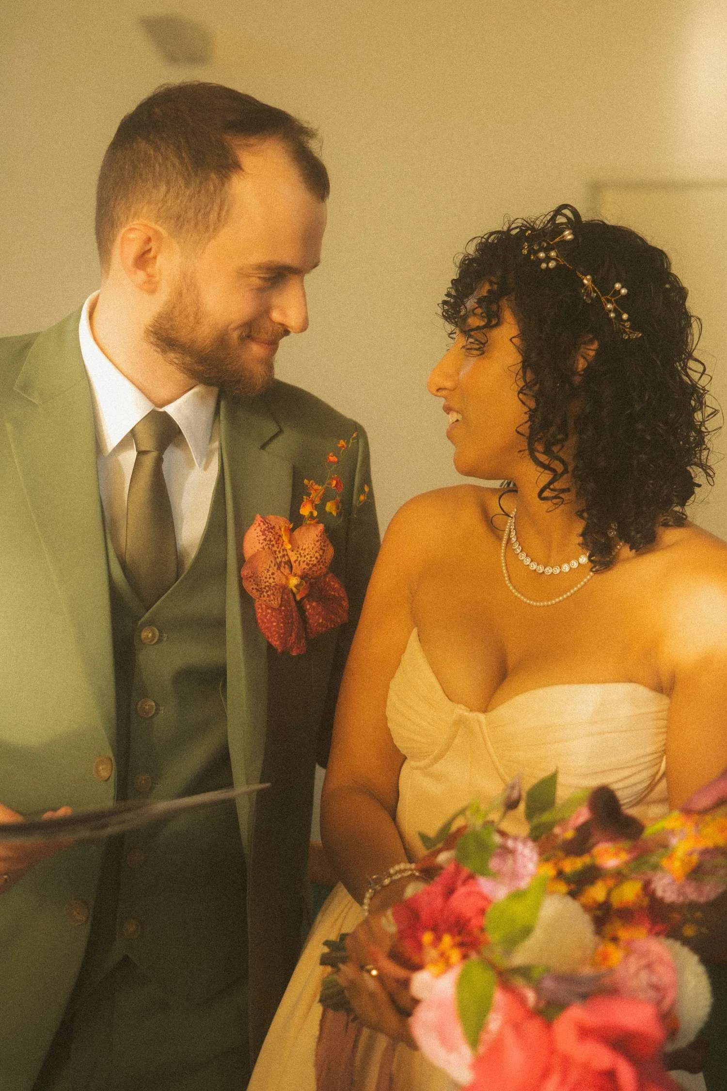 Bride and groom exchanging warm smiles while standing together after signing the marriage documents, holding flowers in soft indoor light.