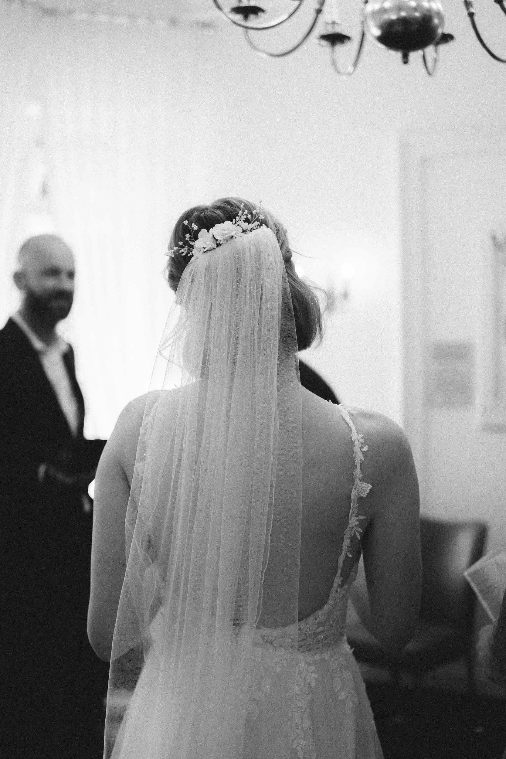 Bride from behind in Berlin Standesamt ceremony room showing floral hairpiece and veil with chandelier