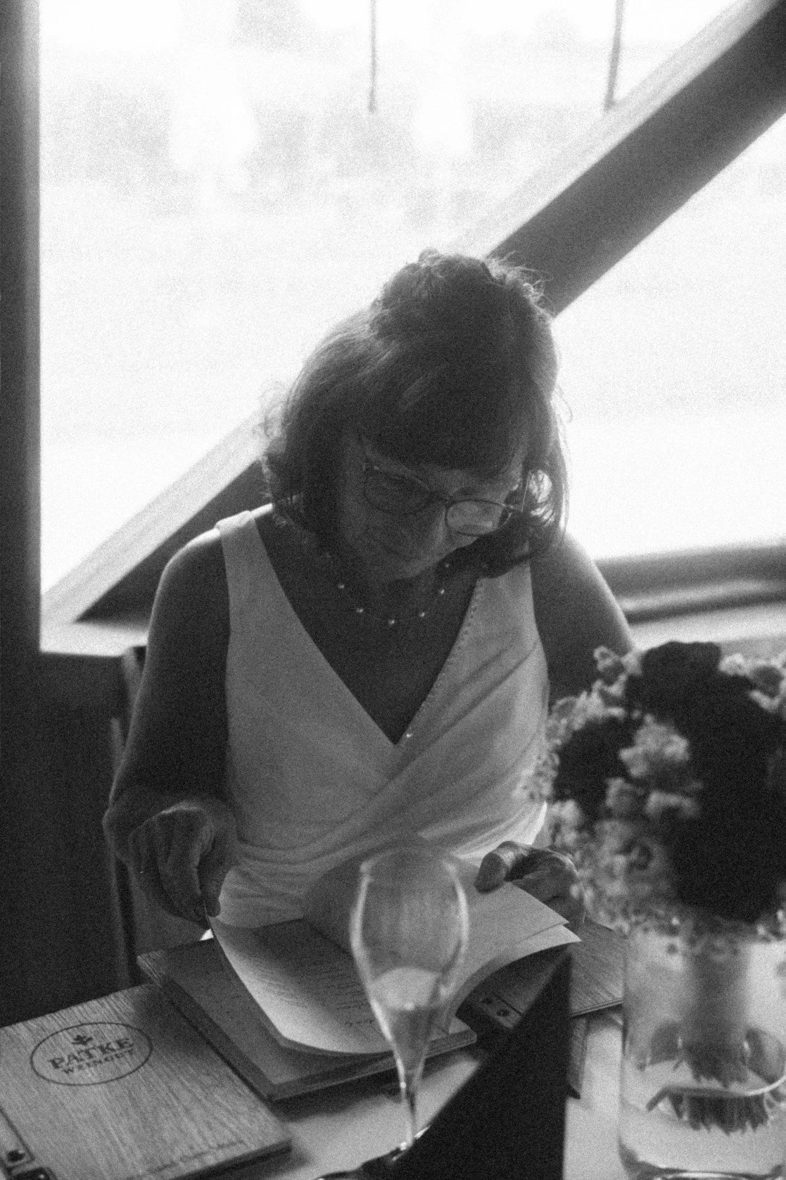 A black and white portrait of a bride in a white dress looking down at a menu at a table.
