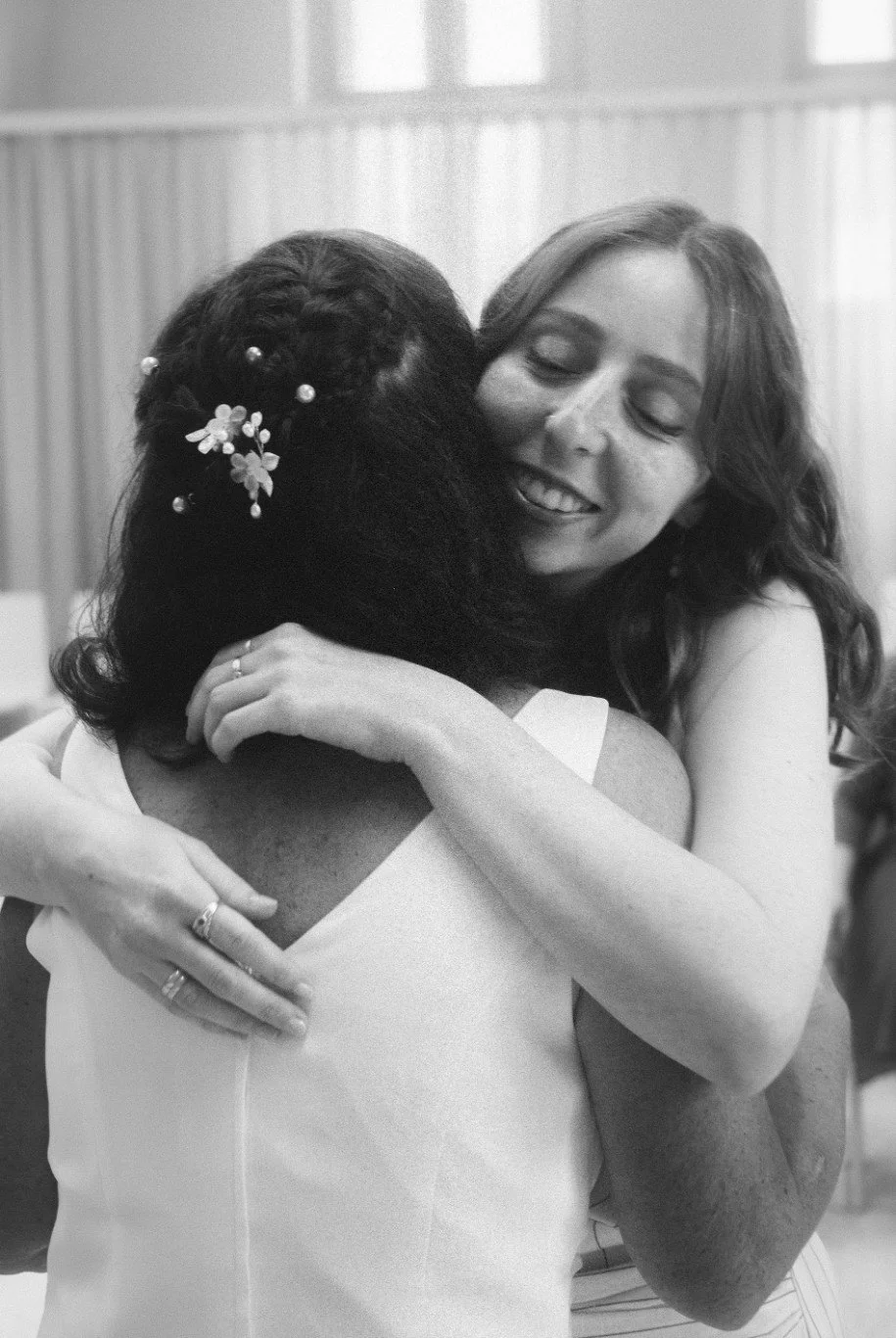 A black and white close-up portrait of a bride smiling while hugging a wedding guest.