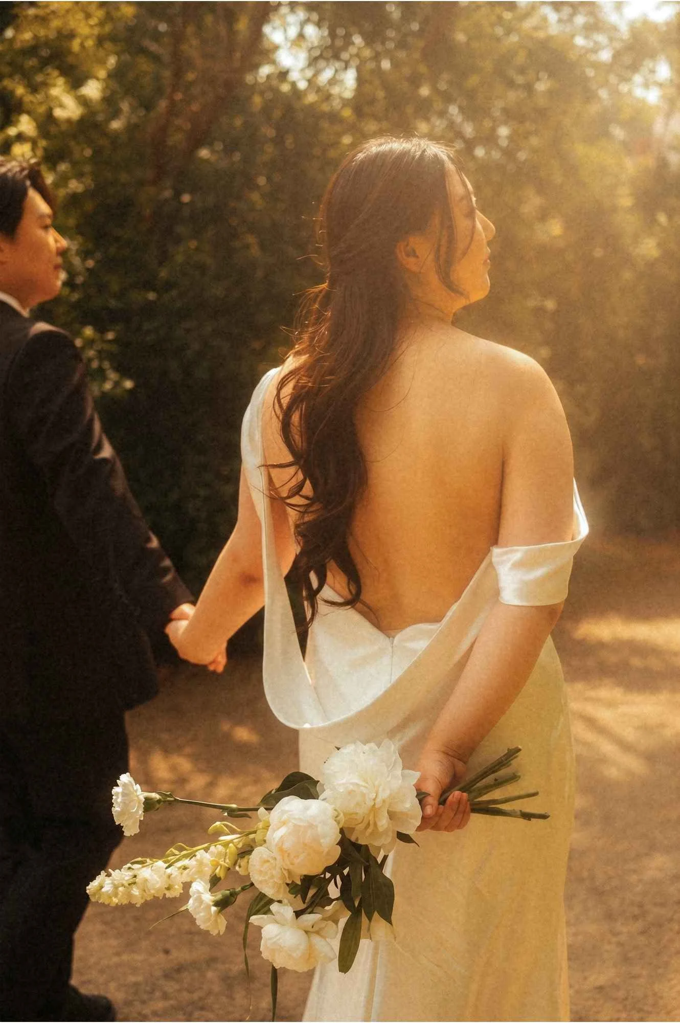 A close-up shot of a bride in a white gown and a groom in black trousers walking side-by-side on a gravel path in Potsdam.