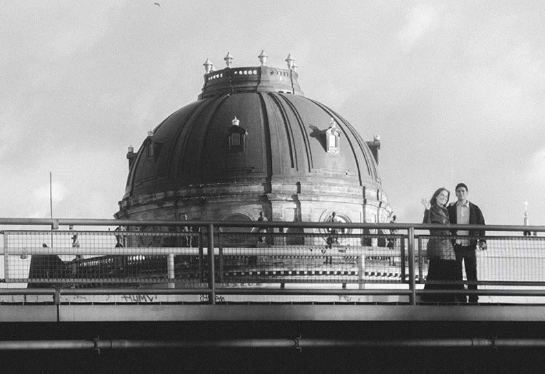 Young couple standing on a bridge in Berlin with the Bode Museum dome in the background, black and white photography.
