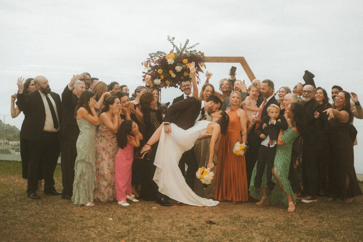 Joyful outdoor wedding group celebrating as the couple shares a kiss during their ceremony in Berlin.