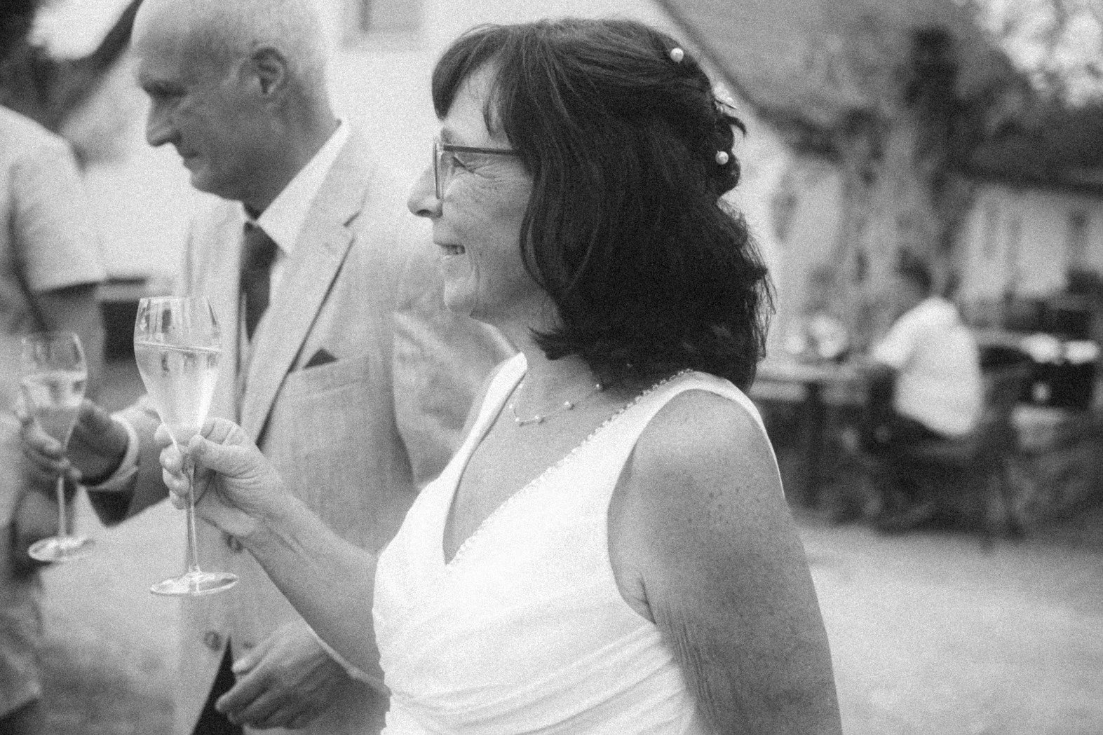 A black and white profile portrait of the wedding couple holding glasses during an outdoor toast.