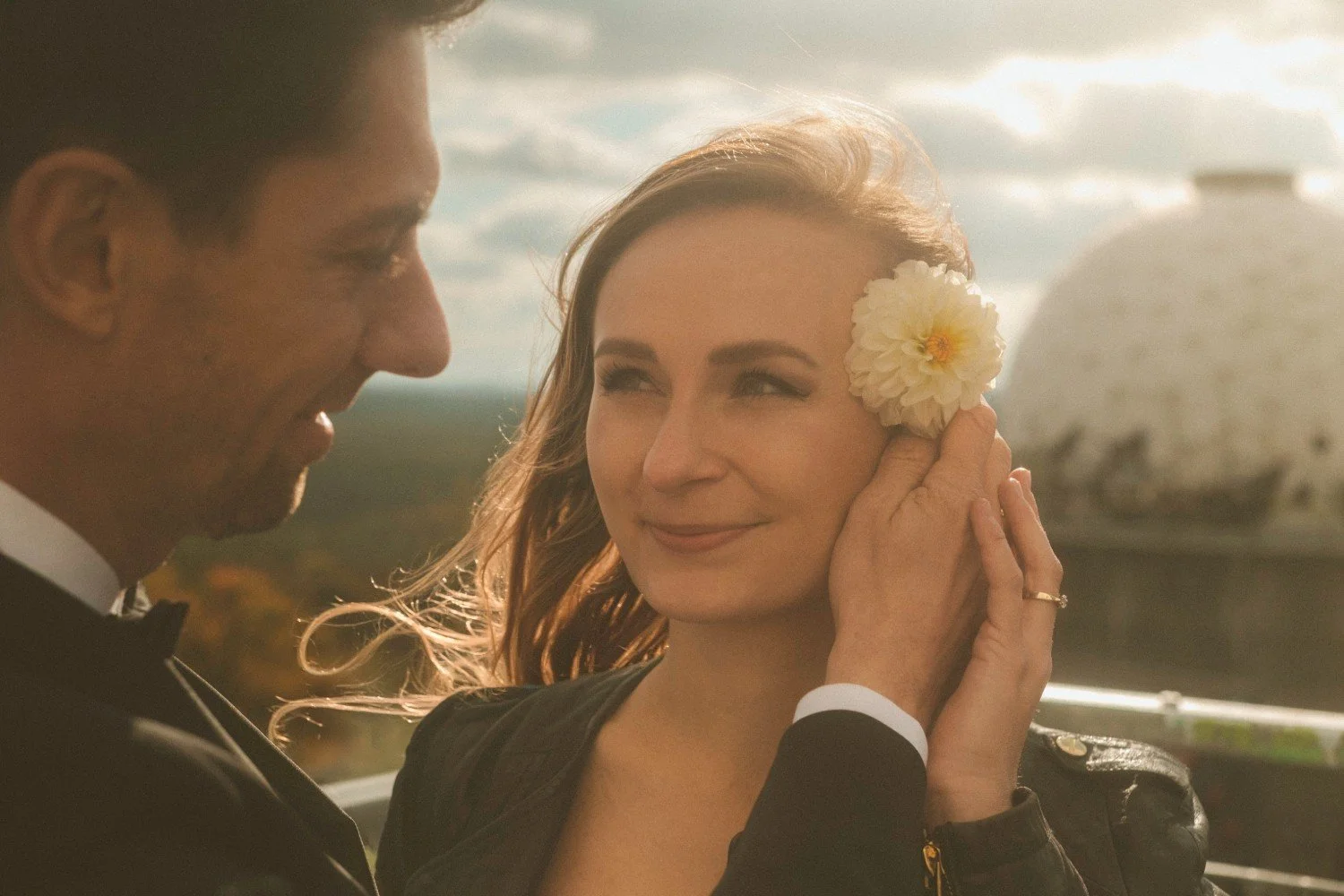 Groom placing white flower in bride’s hair during golden hour wedding photoshoot at Teufelsberg Berlin
