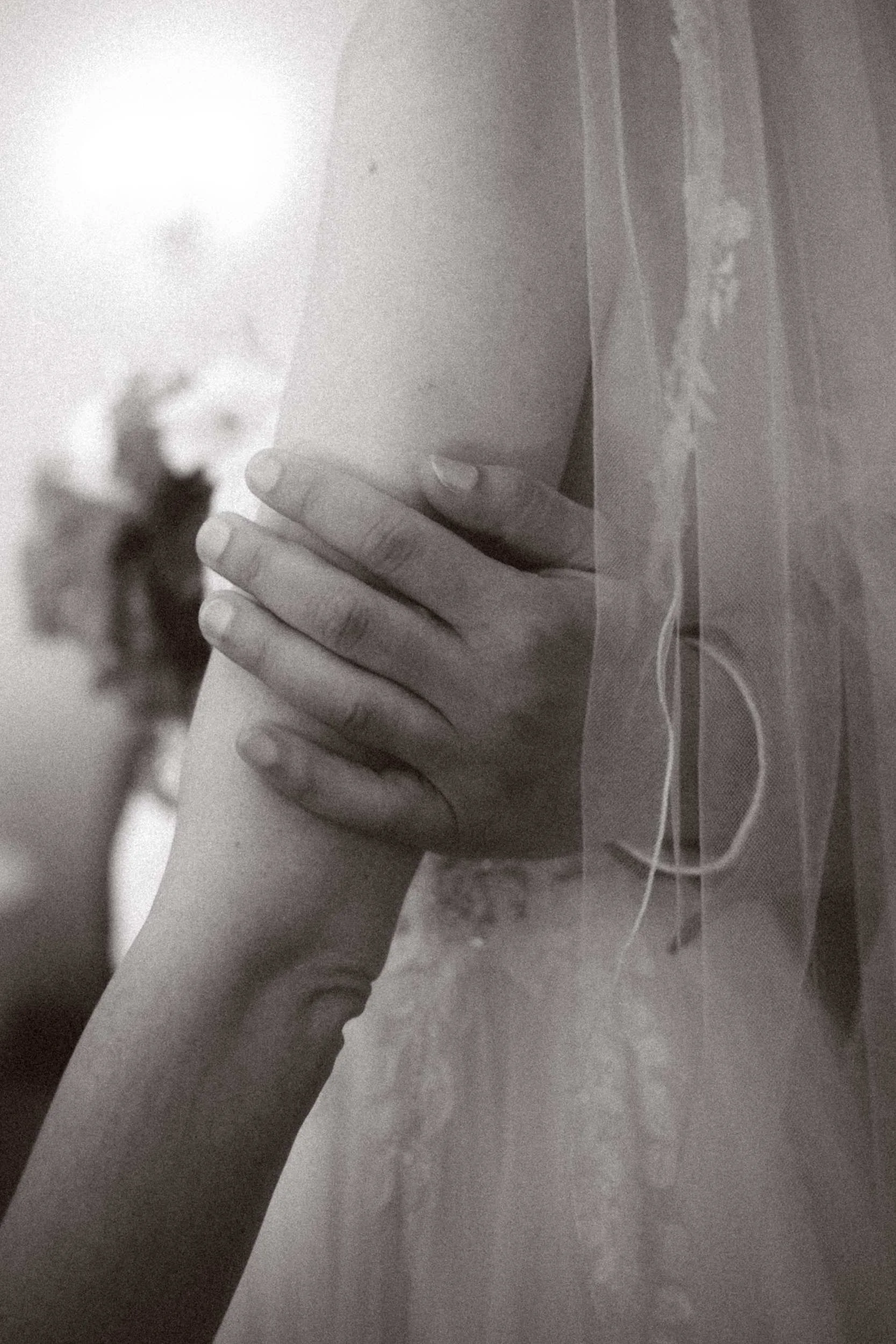 Intimate black and white detail of groom's hands holding bride's arm near her veil at Berlin ceremony