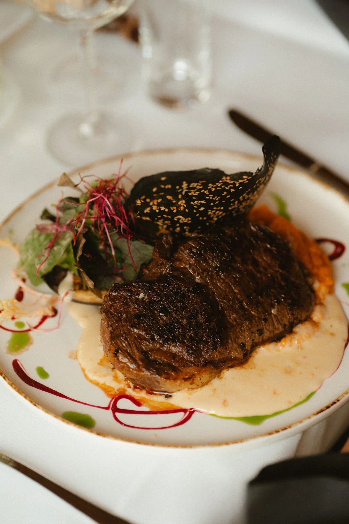 A plated gourmet steak dish with sauce, greens, and a decorative garnish served at a reception.