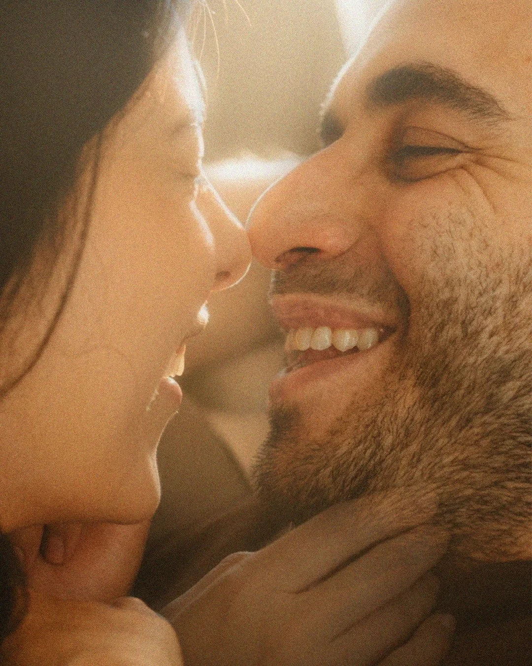 Close-up intimate portrait of a couple smiling face-to-face in a Berlin Kreuzberg apartment with warm light.