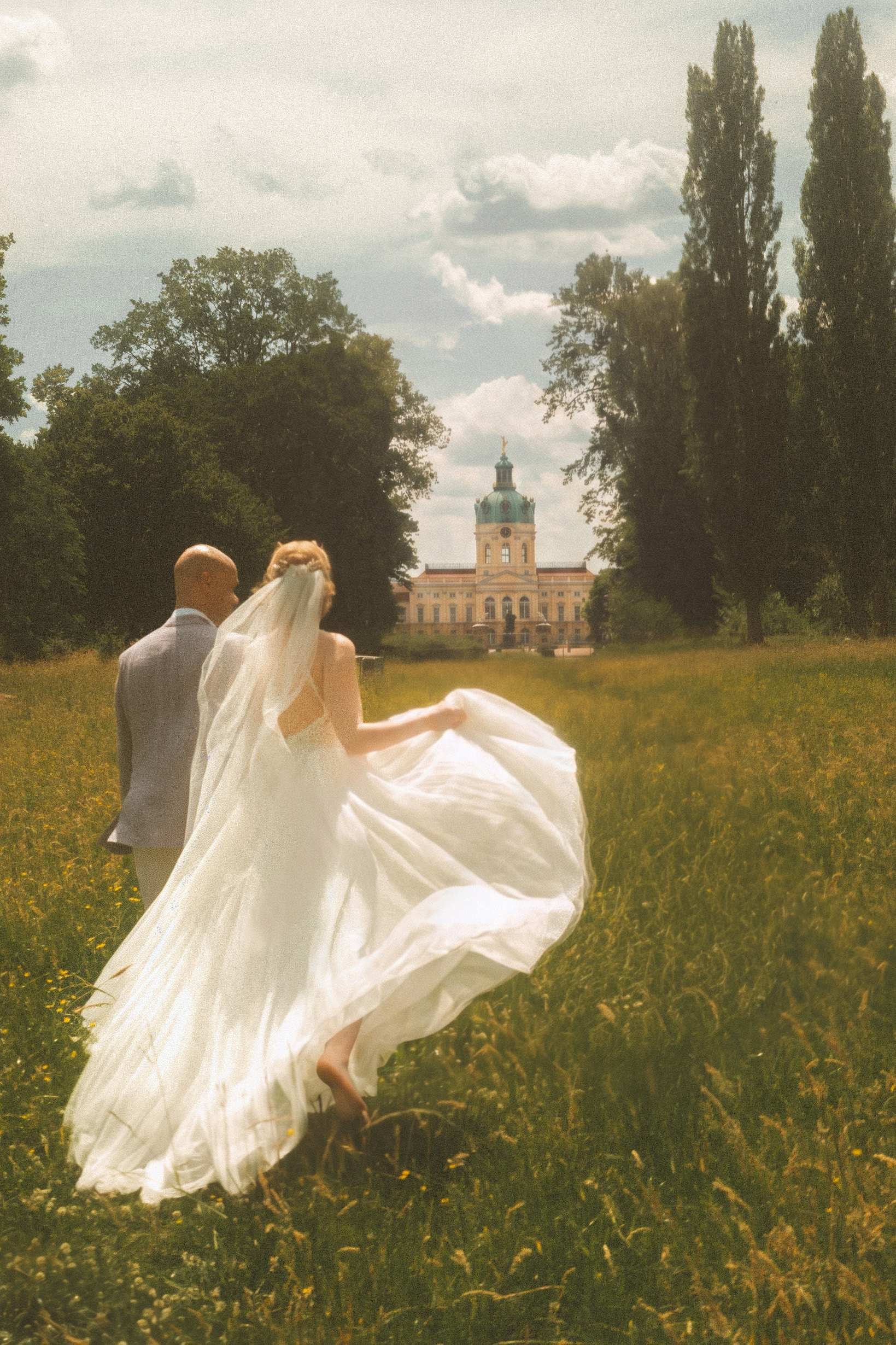 Couple walking hand in hand through meadow toward Schloss Charlottenburg palace, Berlin