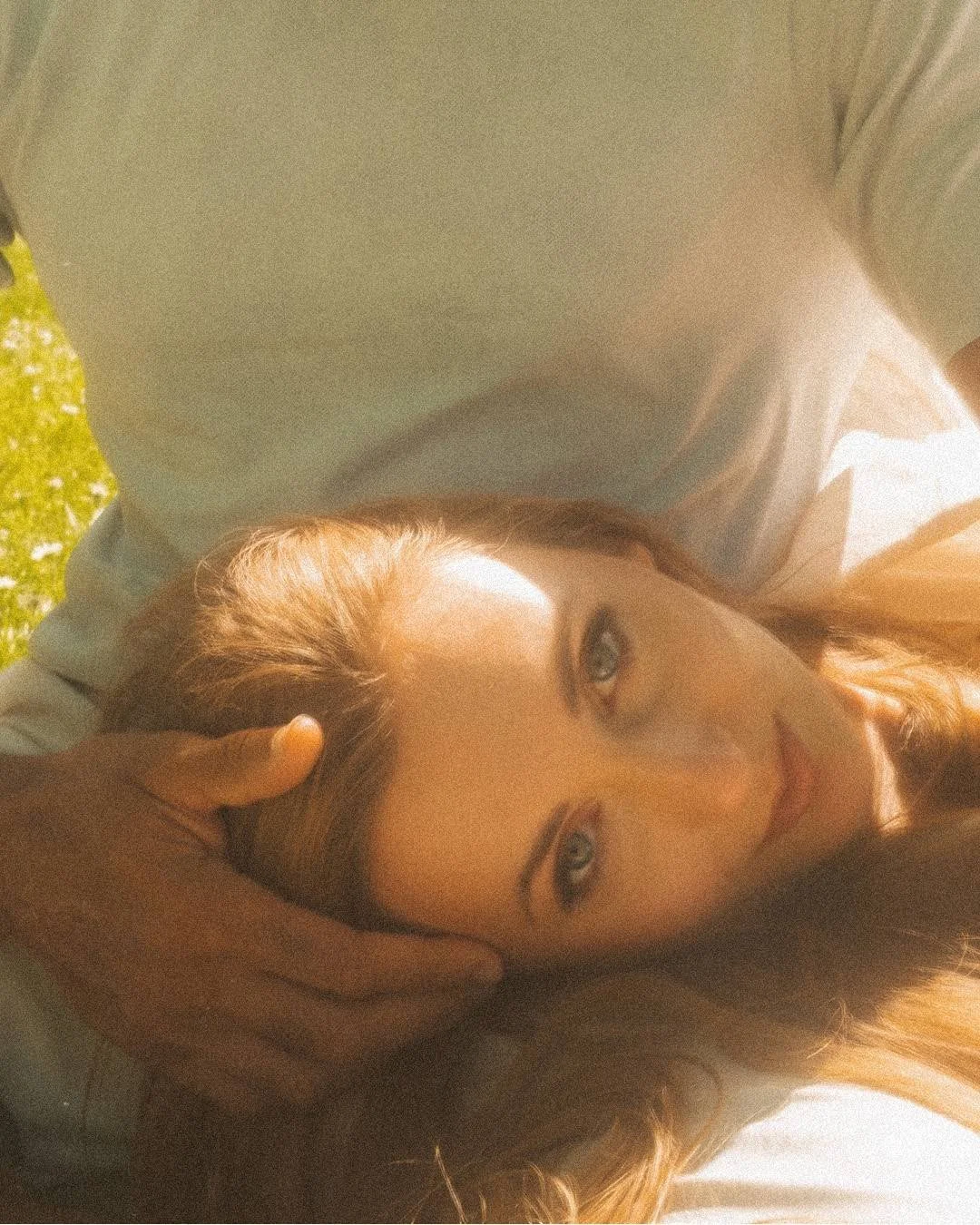 Close up portrait of a woman resting her head on a partner's lap in golden sunlight outdoors in a Berlin park.