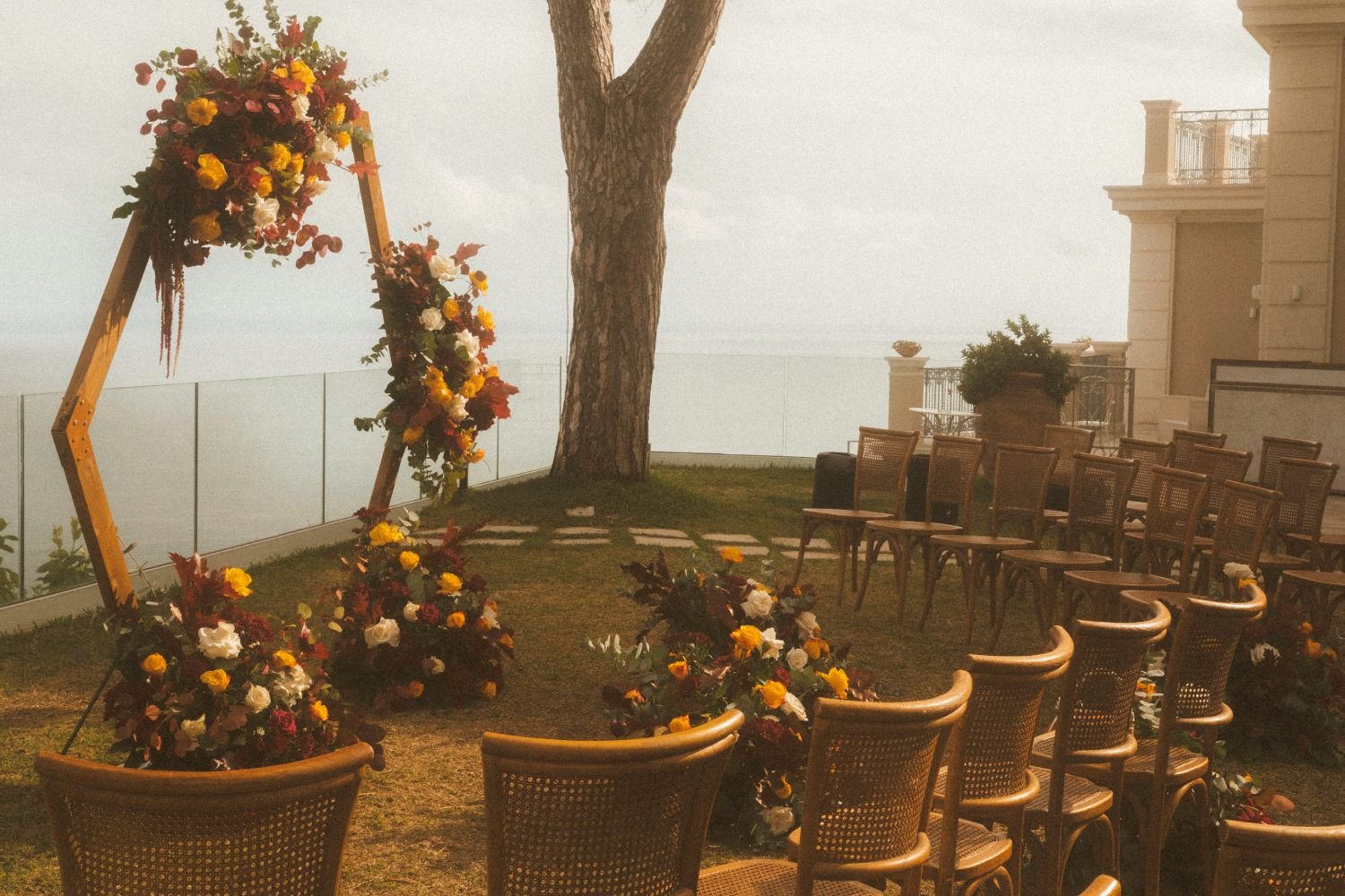 Seaside wedding ceremony setup with floral arch, wooden chairs, and ocean view during an outdoor destination wedding in Italy.