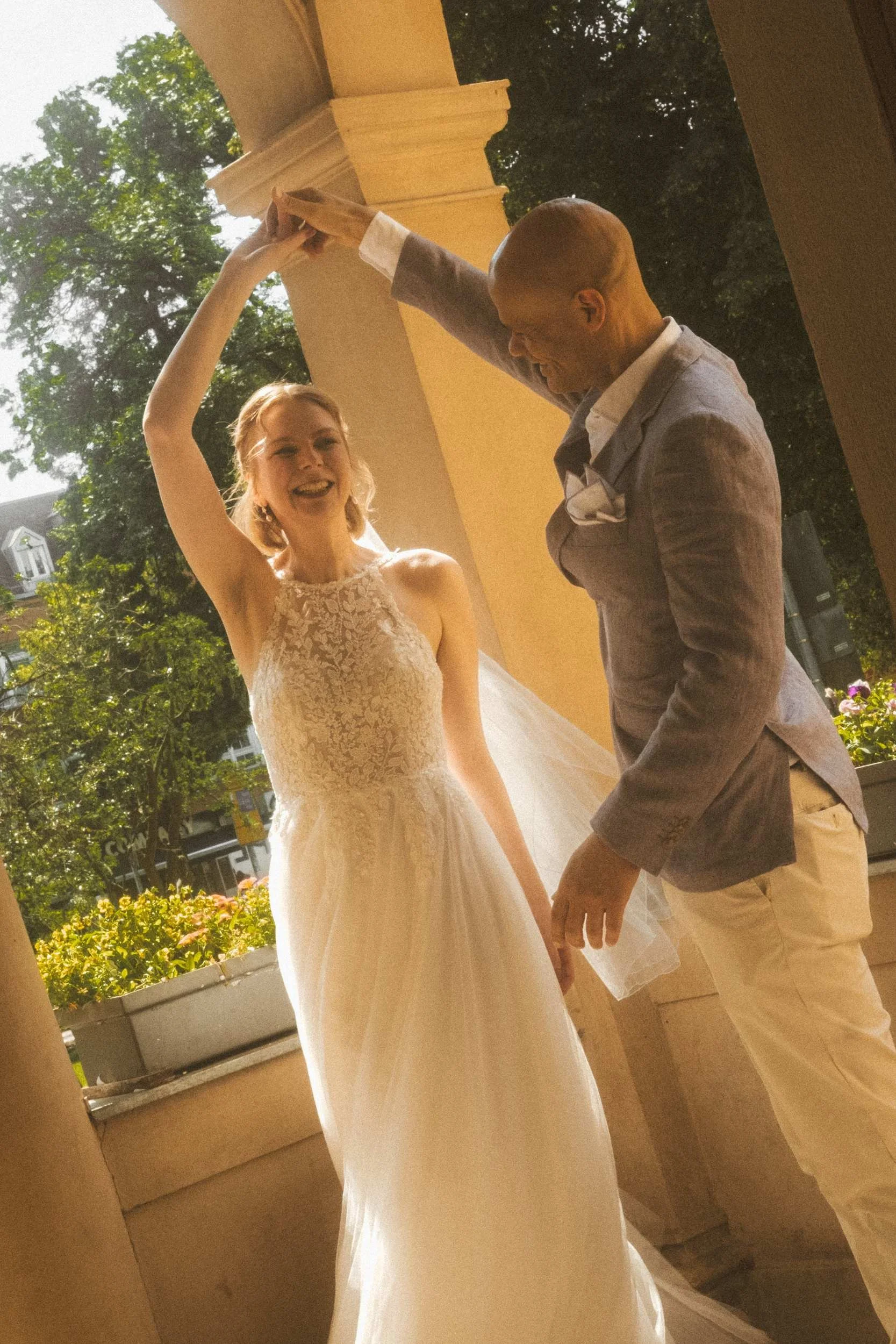 Groom spinning bride under ornate stone arches at Berlin Standesamt in warm afternoon light