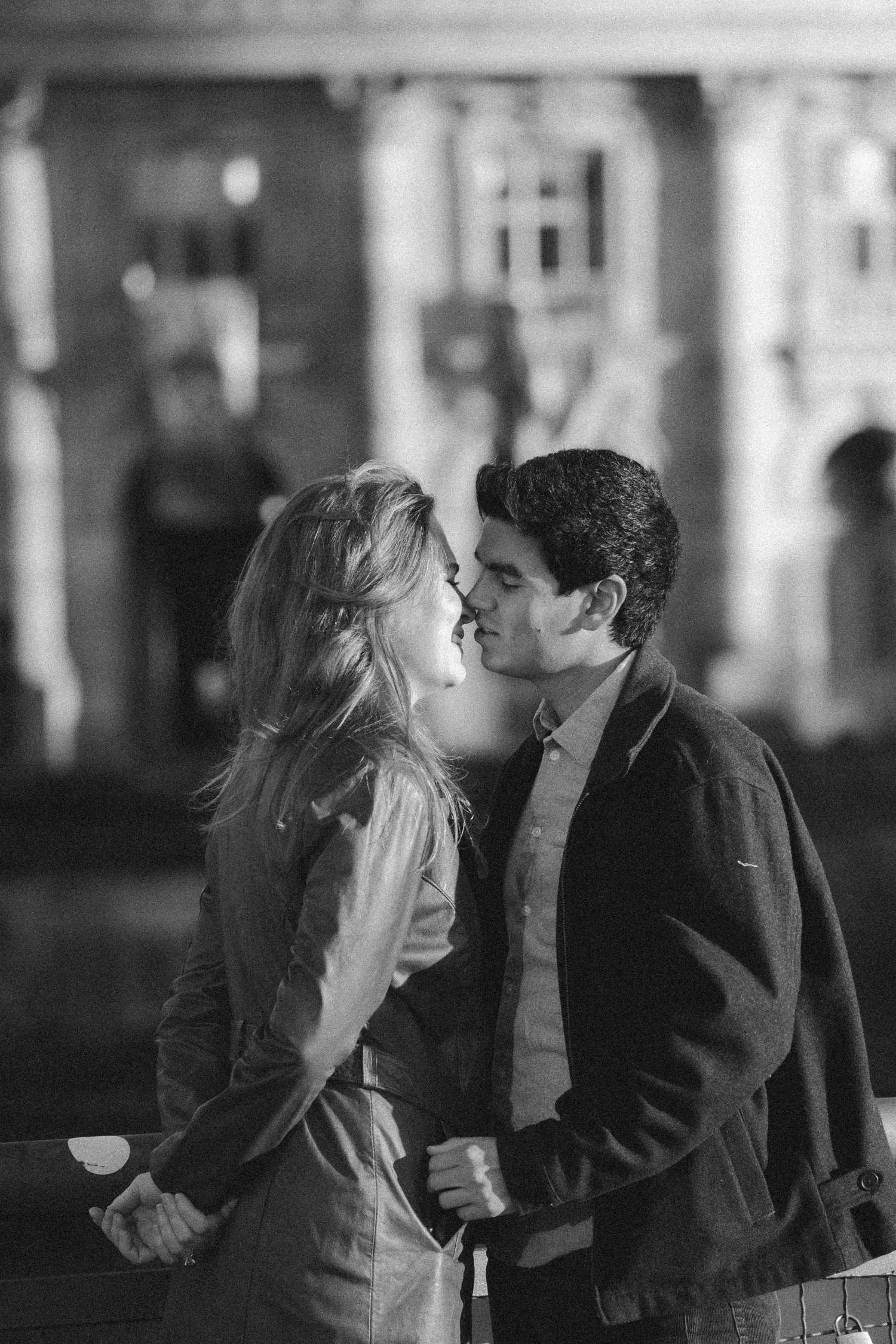 Couple standing close together at night with a museum building lit up behind them in this black and white Berlin engagement photo
