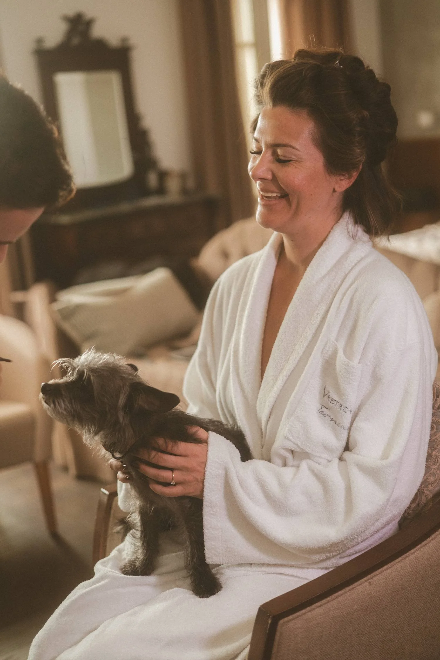 Bride in robe sitting on chair holding her dog during wedding getting ready moment indoors