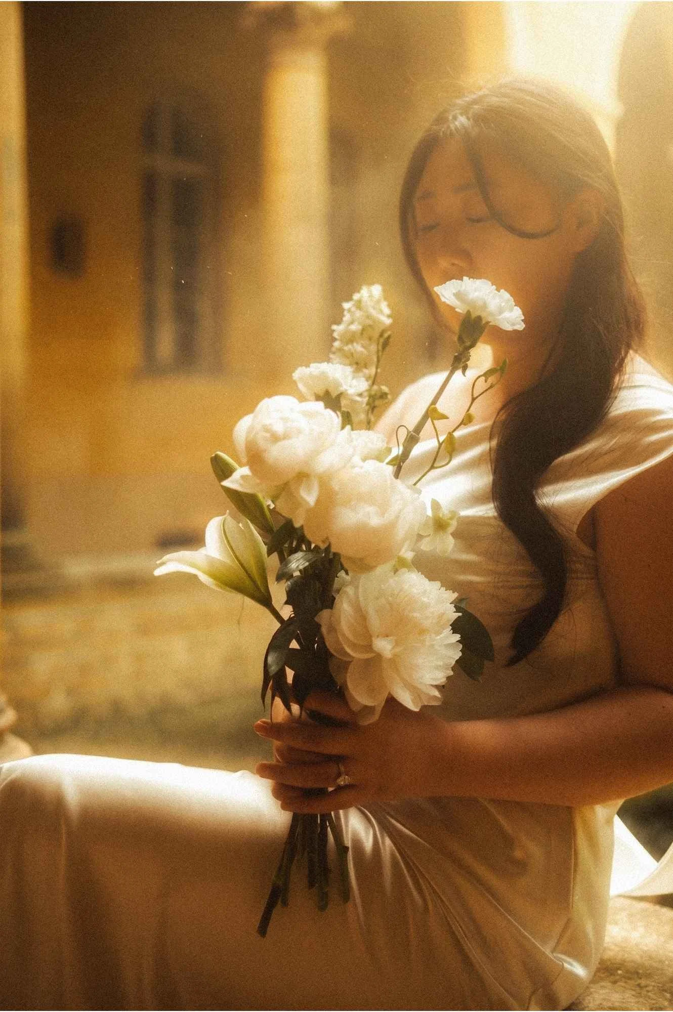 Close-up shot of a bride's hands holding a white floral wedding bouquet with green stems against her white gown in Potsdam.