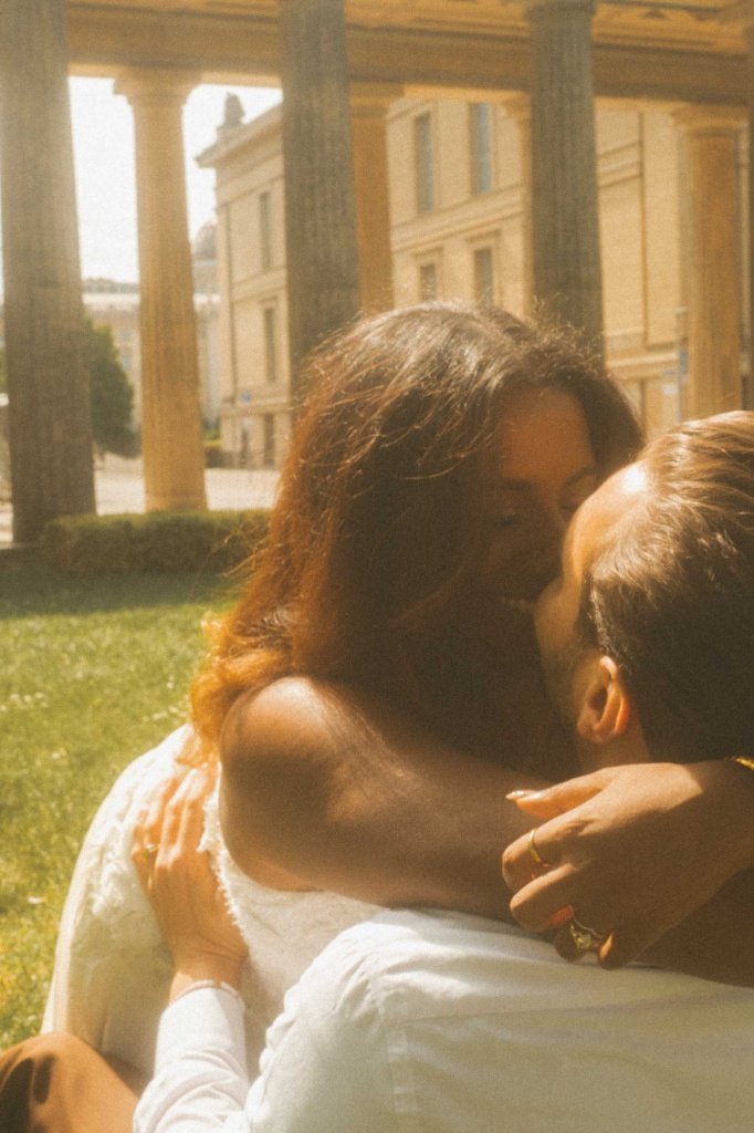 A deeply romantic couple sharing an intimate embrace and kiss in a sunlit park during an engagement photoshoot in Berlin.