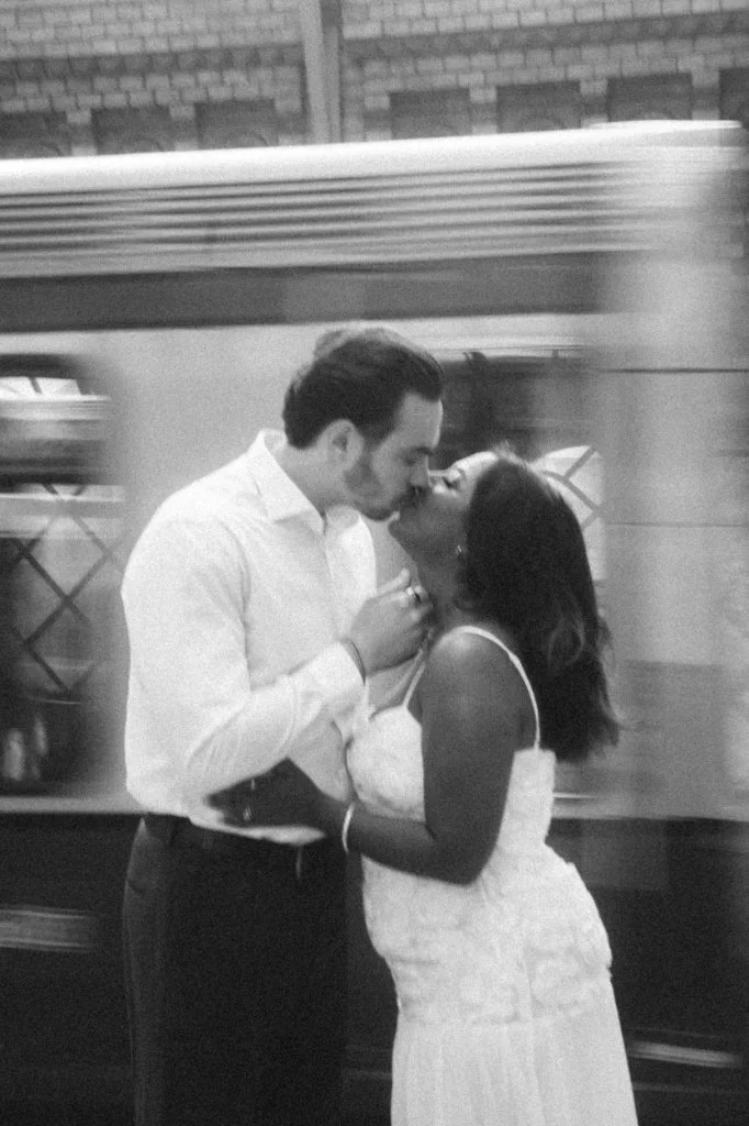 Romantic couple sharing an intimate kiss during an engagement photoshoot in Berlin with cinematic motion blur from a passing train.
