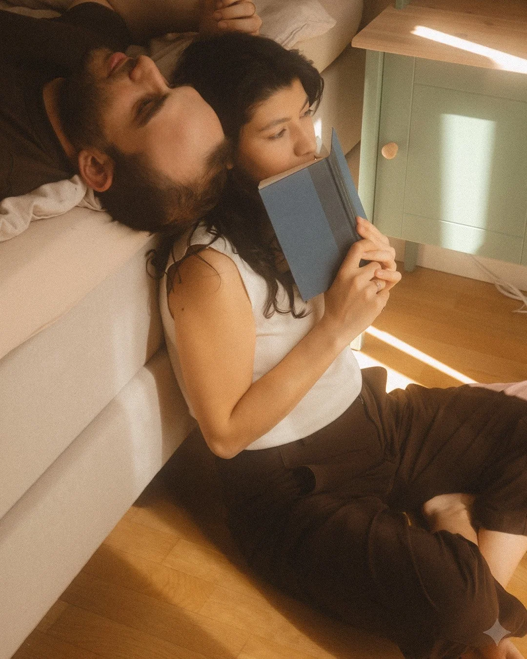 Lifestyle portrait of a couple sitting on the floor of a Berlin Kreuzberg apartment while reading together in sunlight.