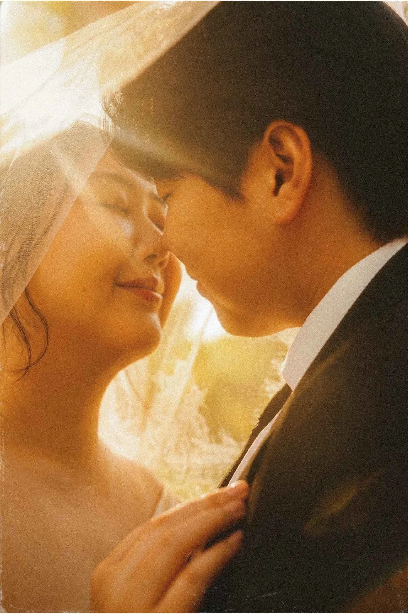 A close-up portrait of a bride and groom smiling and leaning in close to each other in warm, hazy golden hour light outdoors in Potsdam.