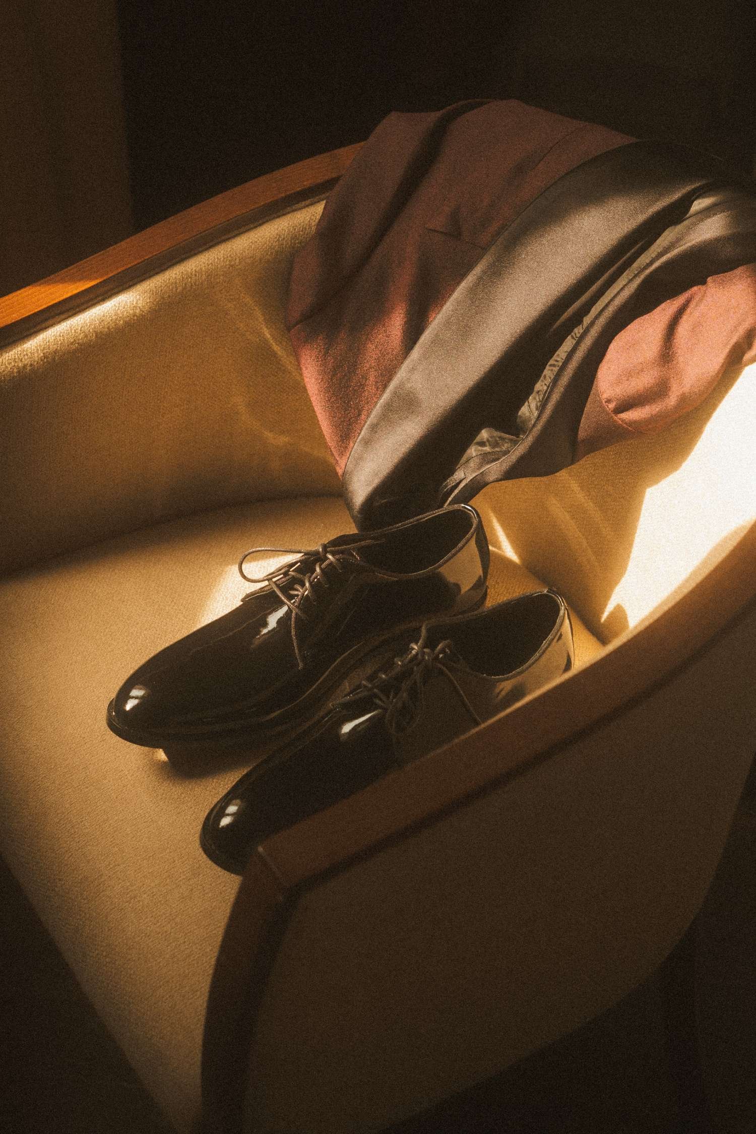 Black patent leather groom shoes with suit jacket on vintage chair, elegant wedding detail photo in Berlin