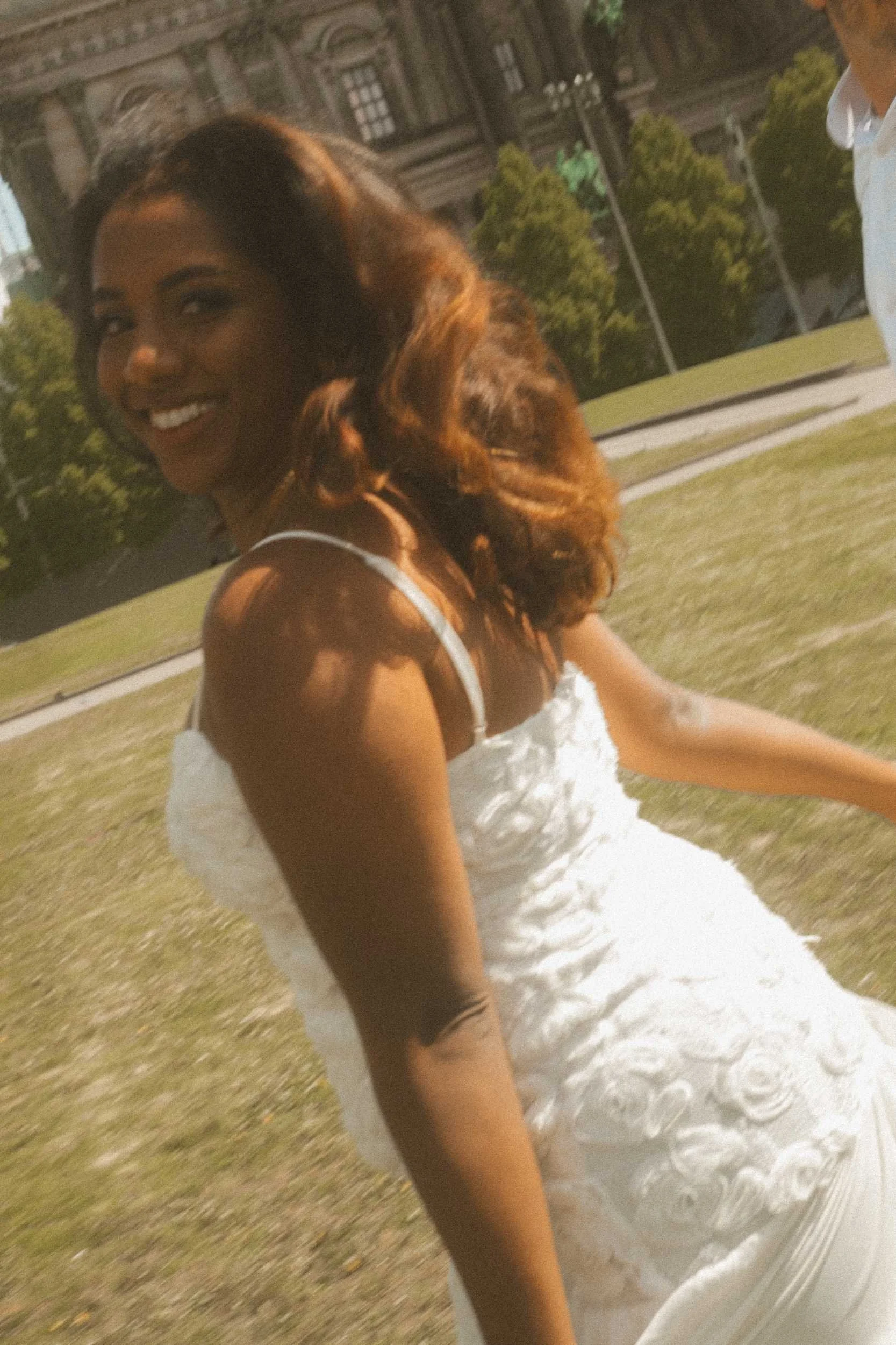 A joyful bride smiling into the camera with a natural sense of motion during a sun-drenched golden hour engagement photoshoot in Berlin.