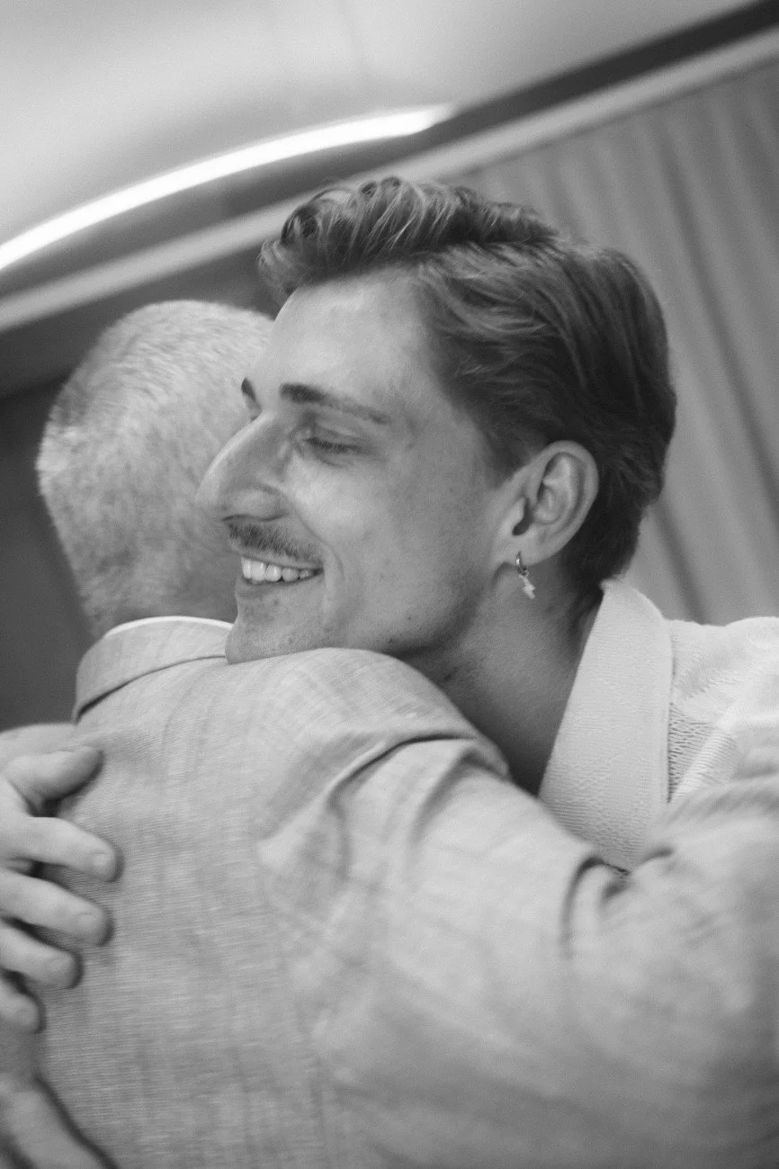 A black and white close-up portrait of a smiling guest embracing the groom.