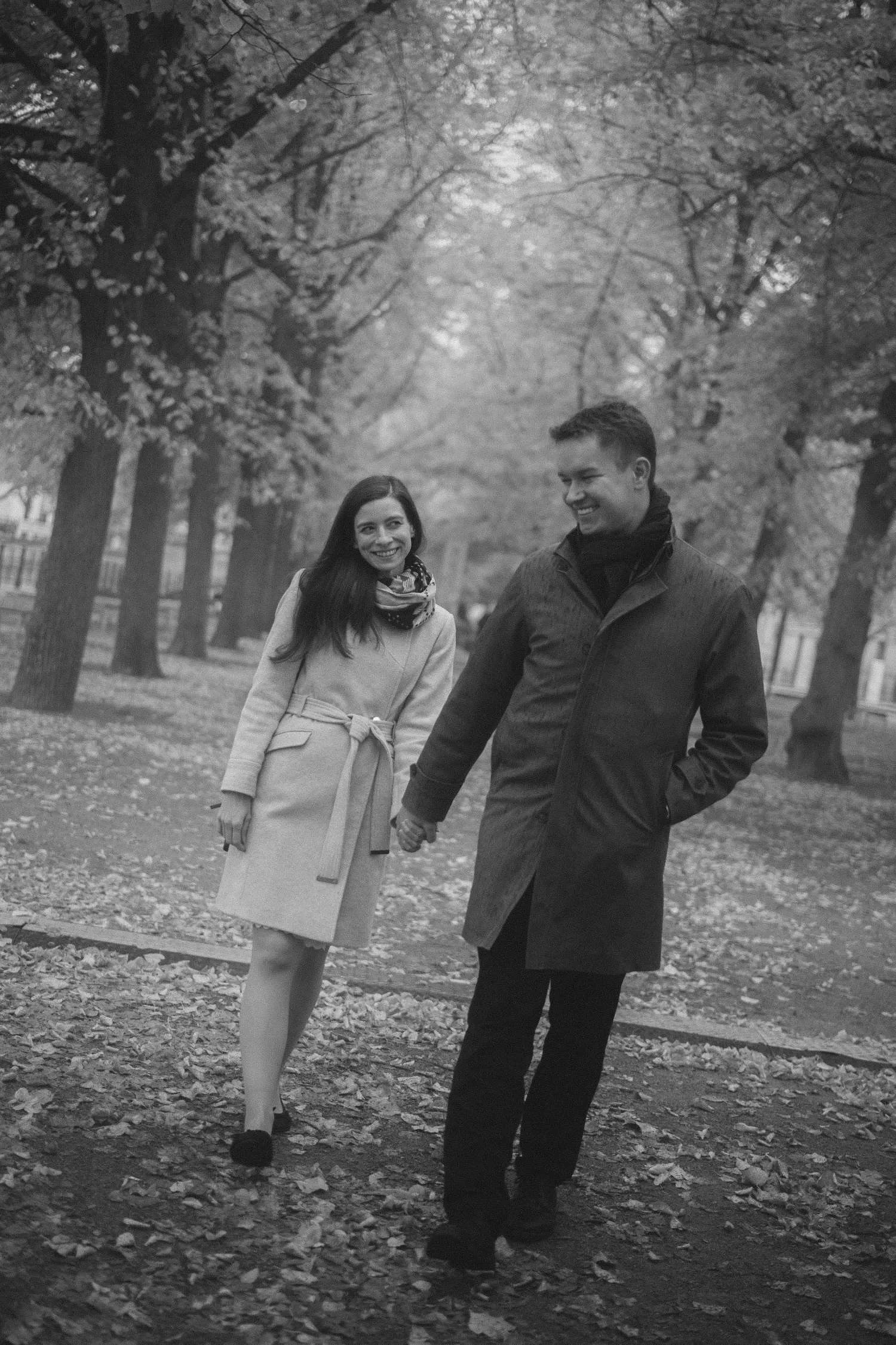 Black and white photo of couple holding hands and walking along tree lined path in Berlin park