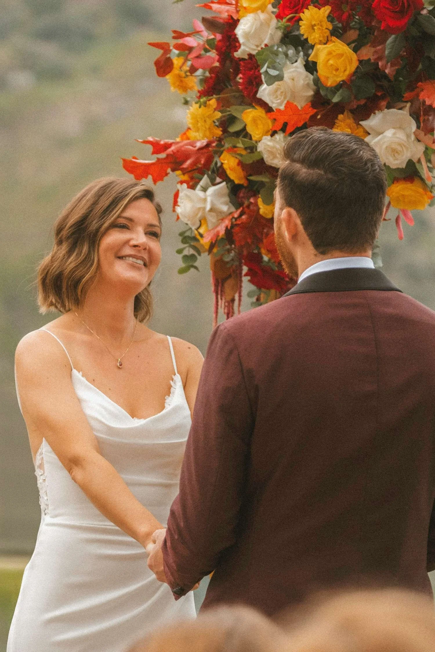 Bride and groom holding hands during an intimate outdoor wedding ceremony with autumn floral arch in Berlin