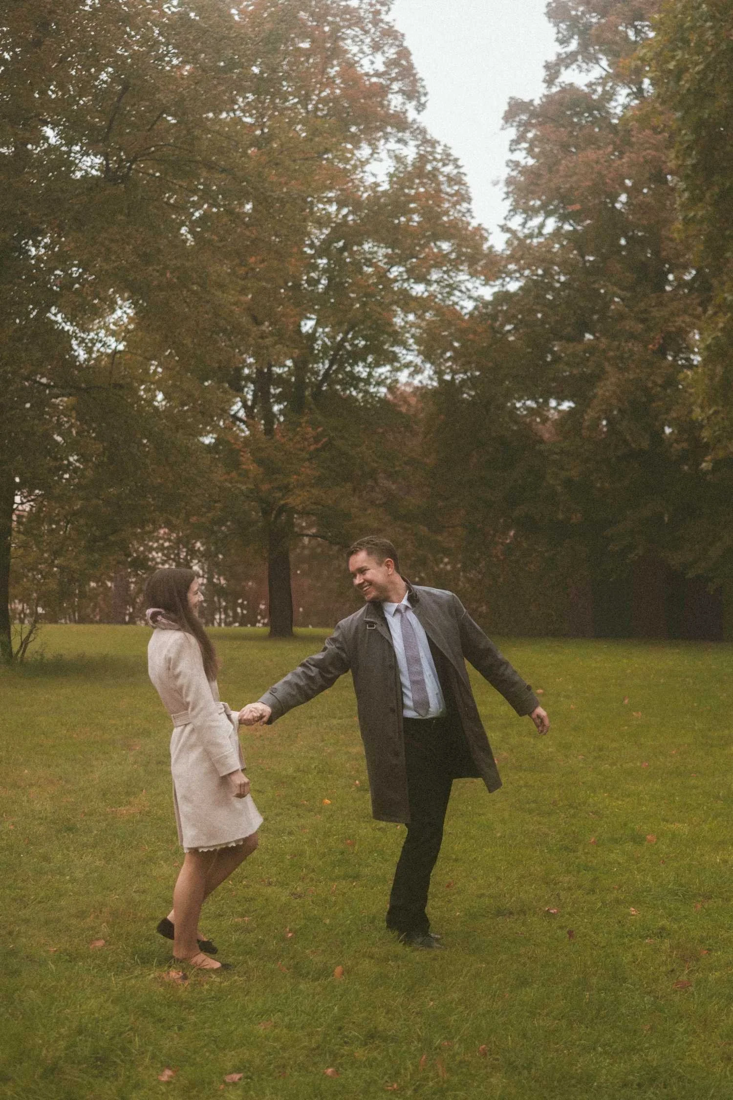 Couple holding hands and spinning on grass in Berlin park during romantic outdoor photoshoot