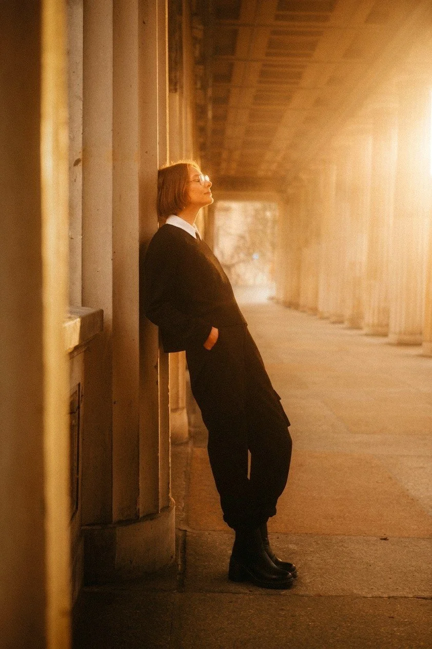 A side-profile of a woman in black clothing leaning against a large column during golden hour in Berlin.