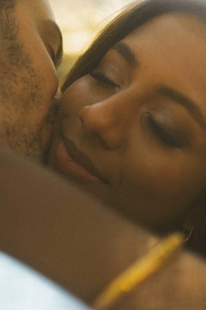 An intimate close-up portrait of a bride with eyes closed, receiving a tender kiss on her cheek from the groom during an engagement photoshoot in Berlin.