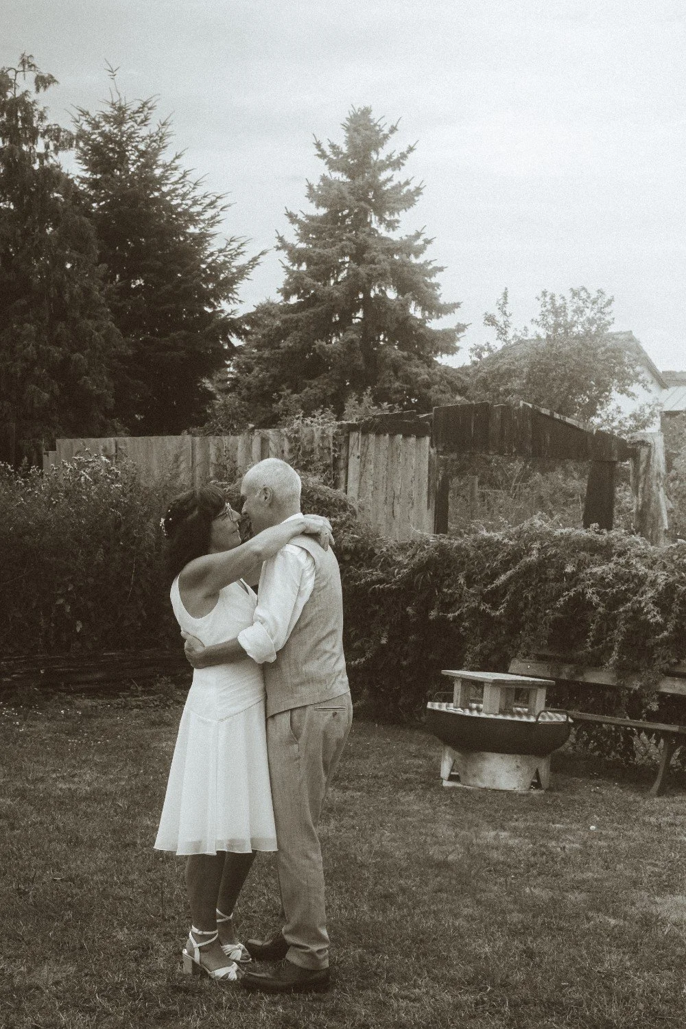 A medium black and white outdoor shot of the wedding couple dancing together in a garden.