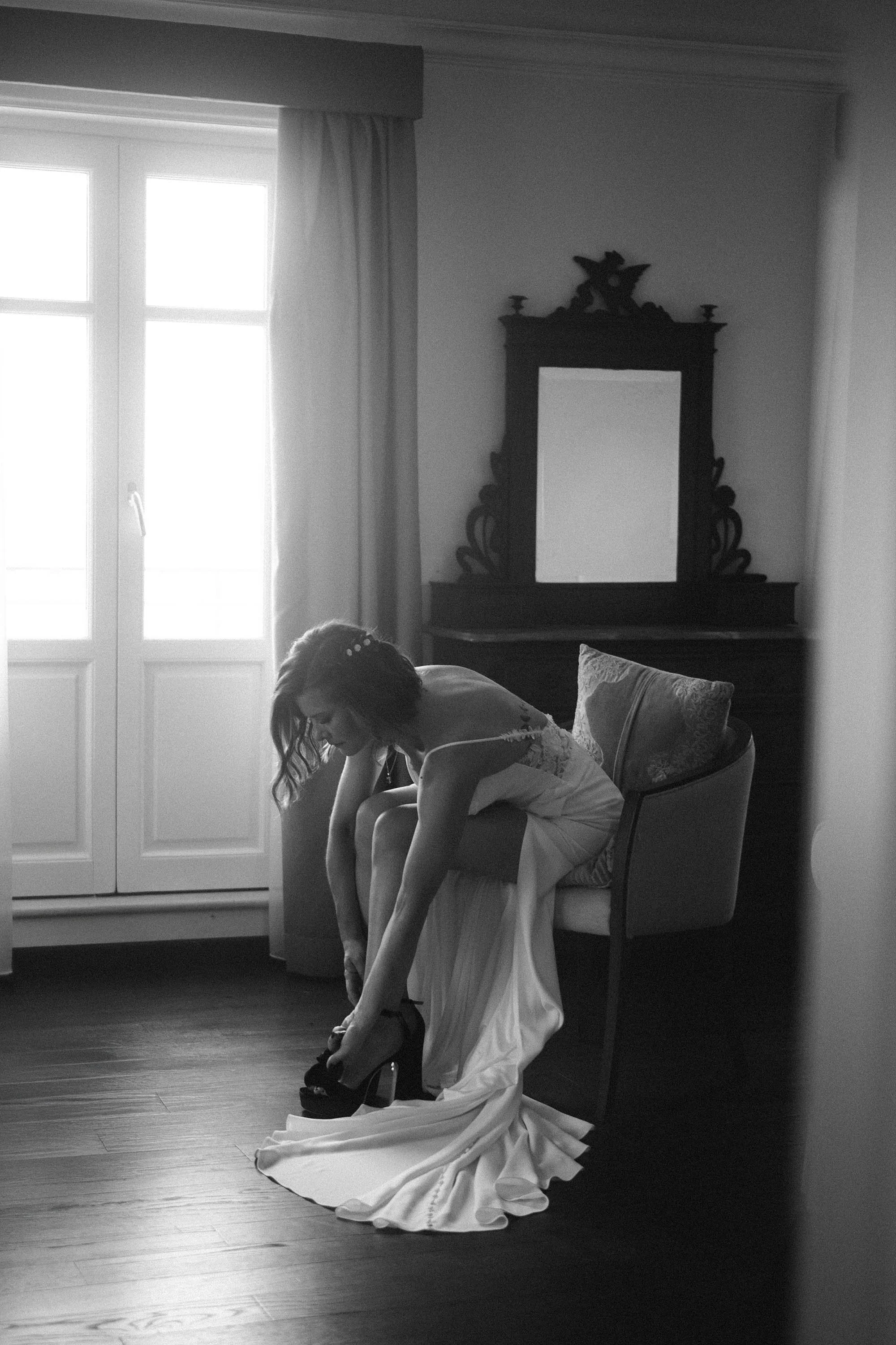 Bride putting on her heels during wedding morning preparations in Sicily, quiet black and white getting-ready moment.