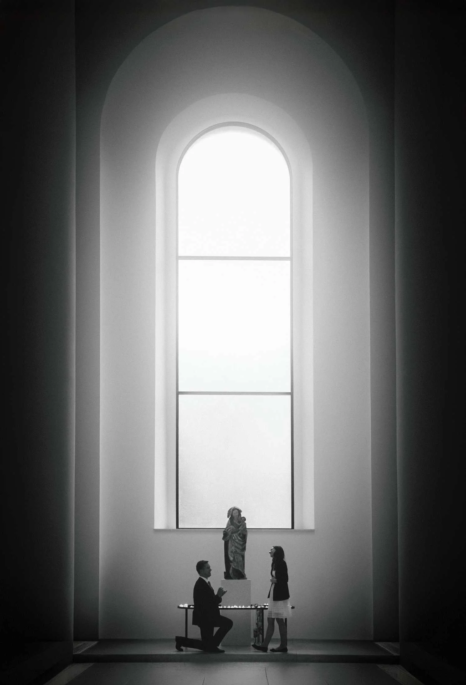 Man kneeling during proposal in front of tall church window in Berlin during romantic photoshoot