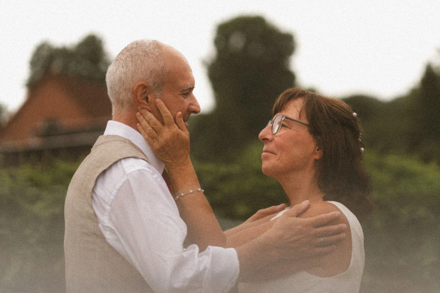 A close-up outdoor profile shot of the wedding couple looking at each other lovingly, with the bride holding the groom's face and shoulders.