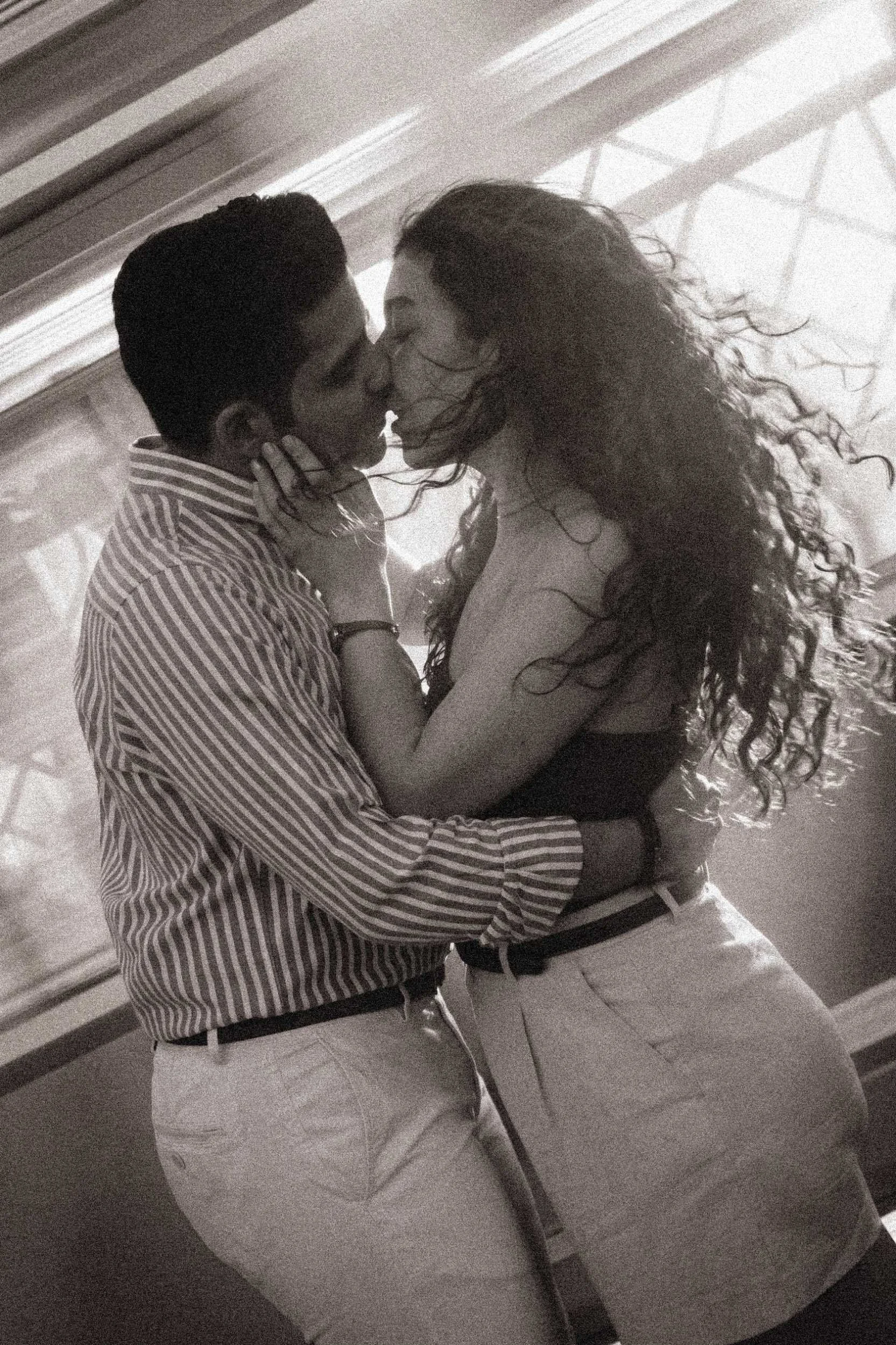 A cinematic, black-and-white engagement portrait of a couple kissing while captured with a motion blur effect from a passing train in Berlin.