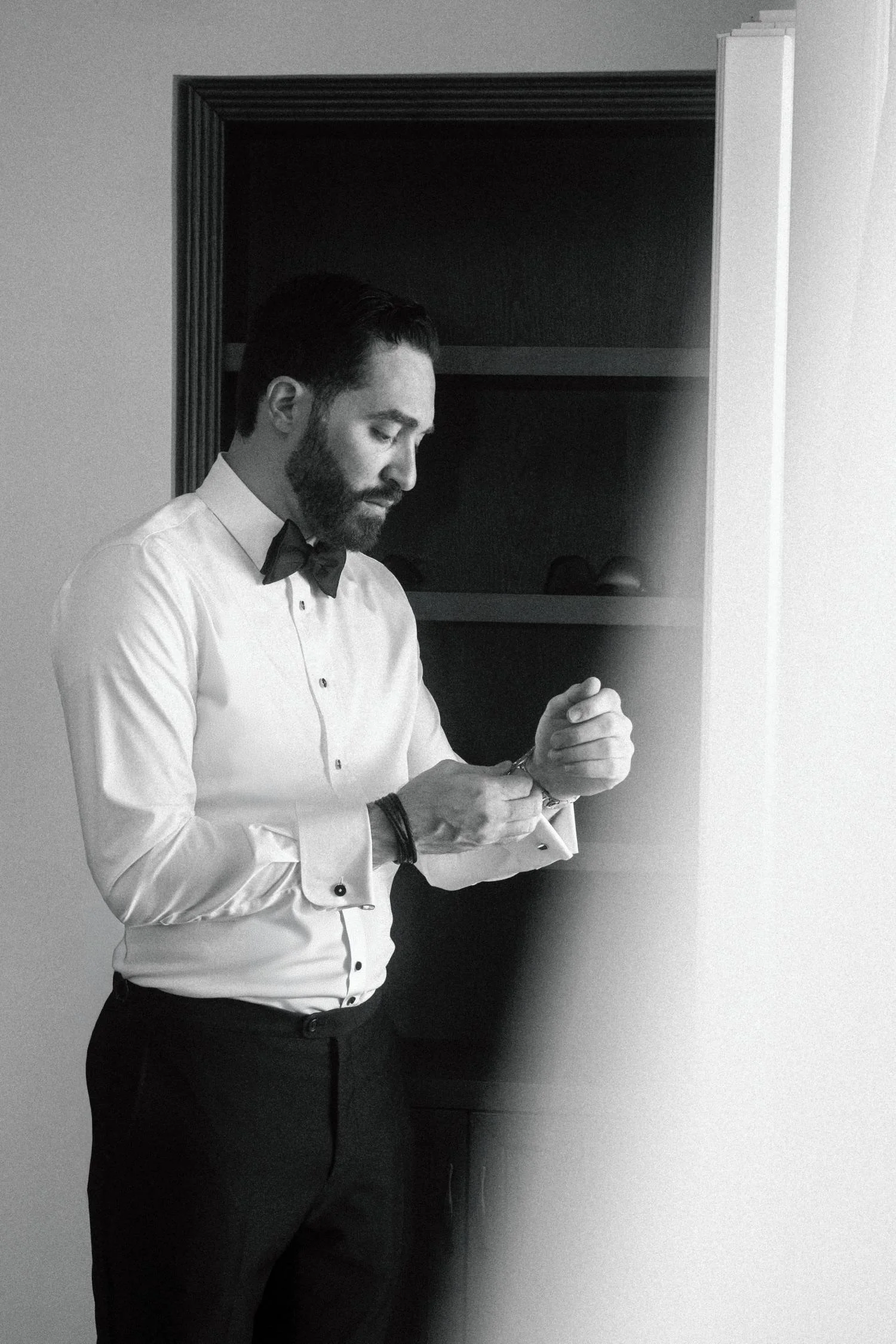 Black and white portrait of groom adjusting cufflinks while getting ready for wedding indoors