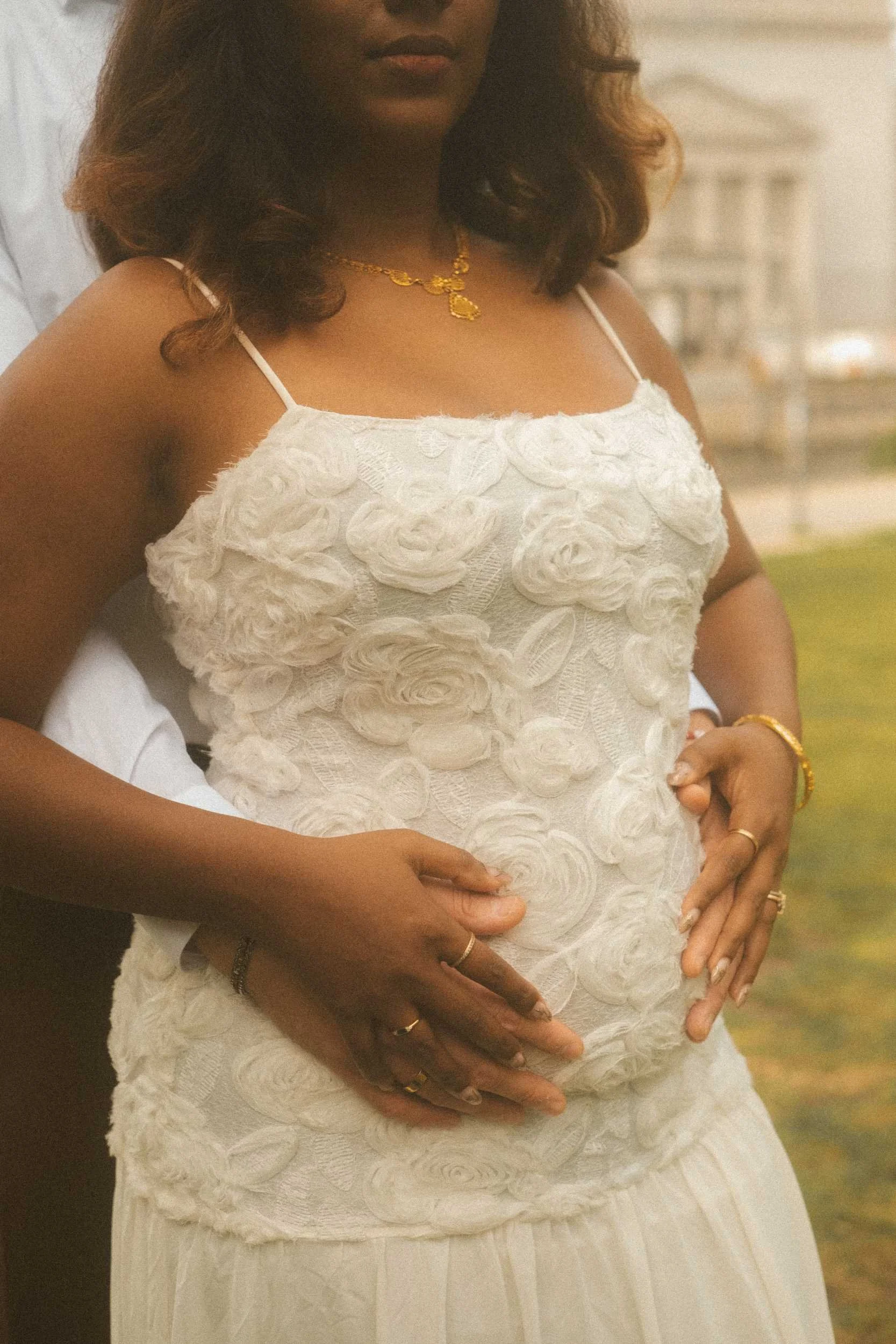 A close-up engagement portrait in Berlin, featuring a man embracing the woman from behind with his hands on her stomach and her hands resting over his.