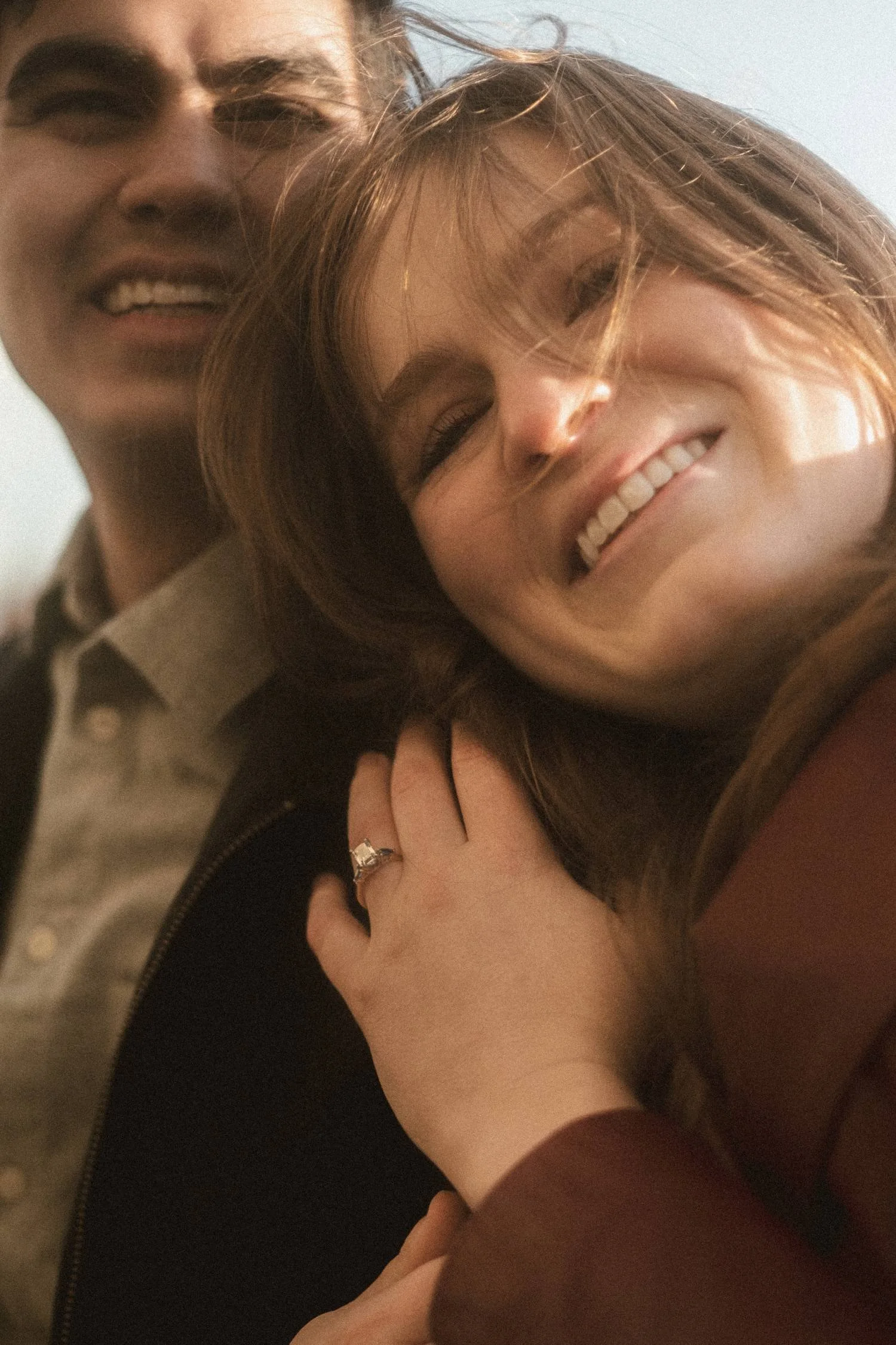 Engaged couple smiling closely together during an outdoor photoshoot in Berlin, showing an engagement ring in natural light