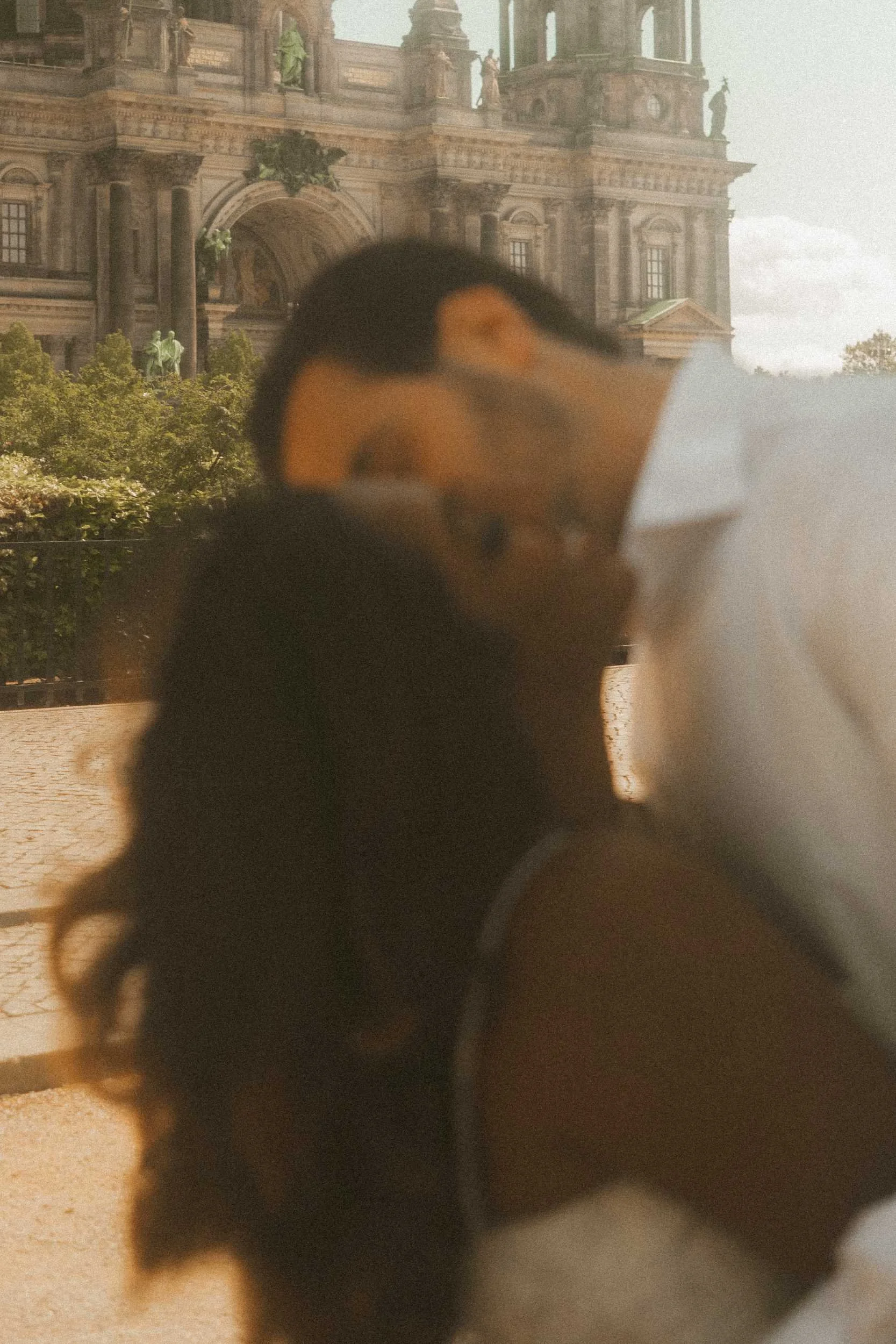 An artistic, blurry engagement portrait of a couple in Berlin, capturing the groom kissing the bride on the cheek with her head tilted back and eyes closed, set against the historic cathedral.