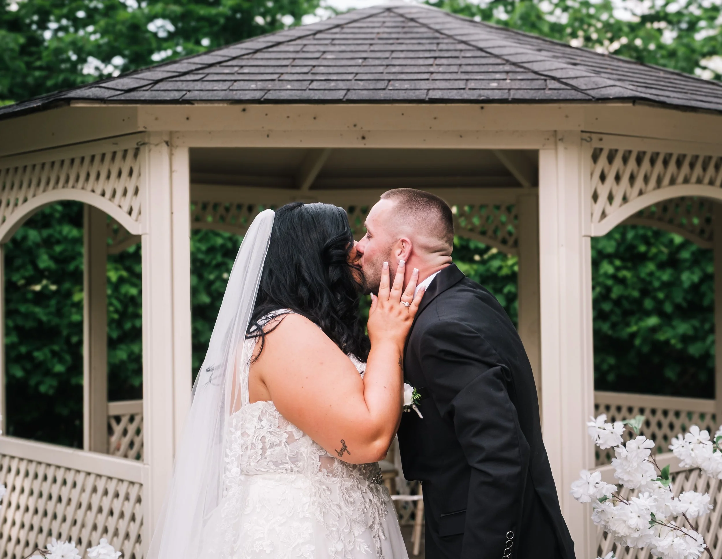 Bride and groom sharing a kiss during their wedding in a gazebo with white flowers in the foreground.