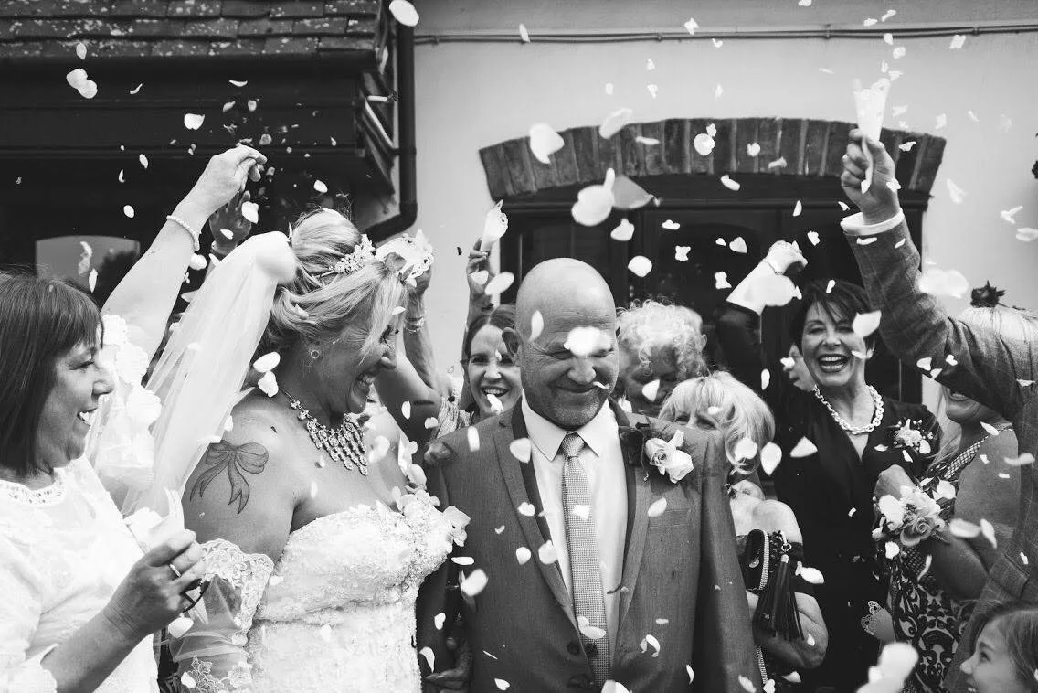 A wedding celebration with a bride and groom surrounded by guests throwing confetti.