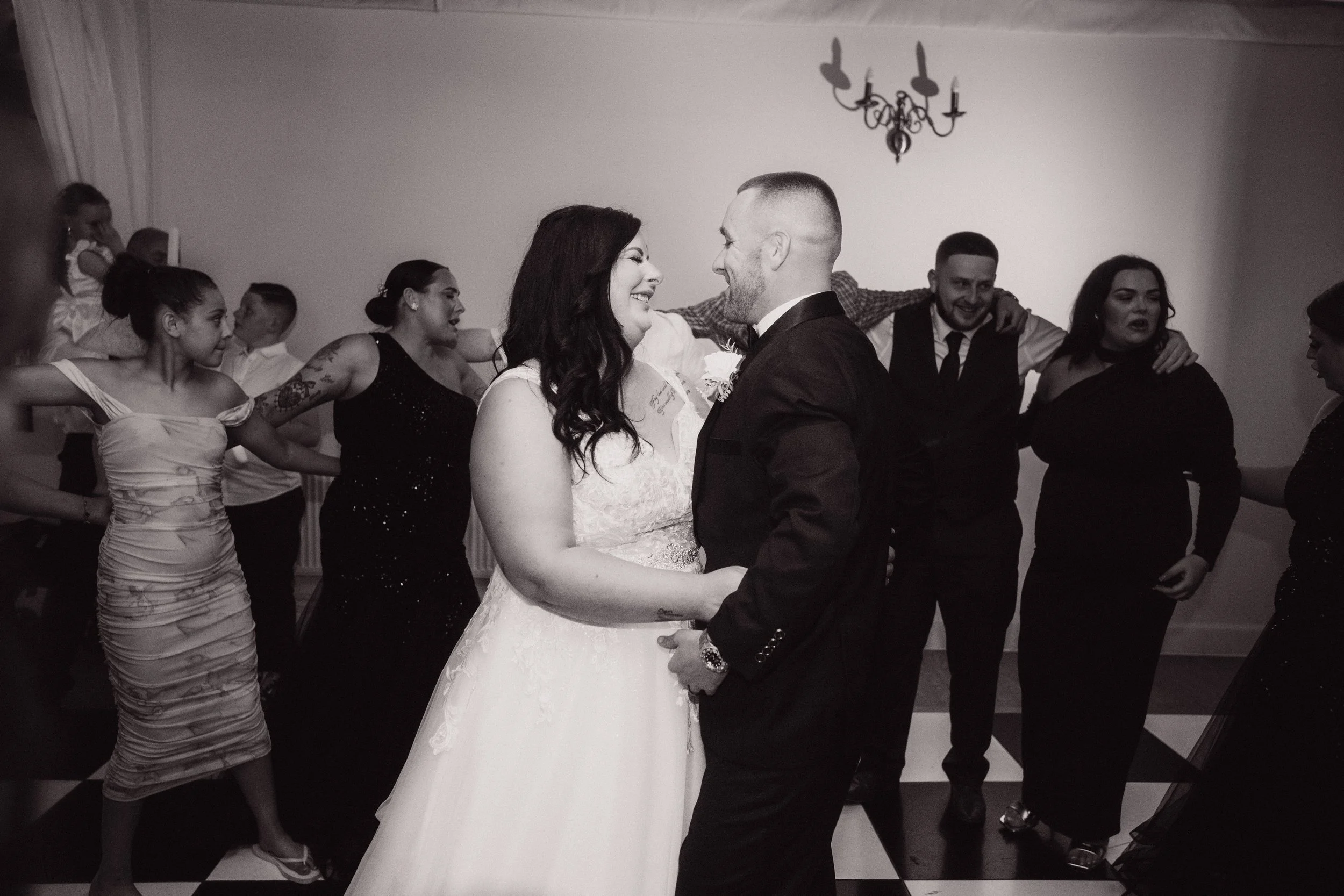 Couple in wedding attire dancing with guests in the background at a wedding reception.