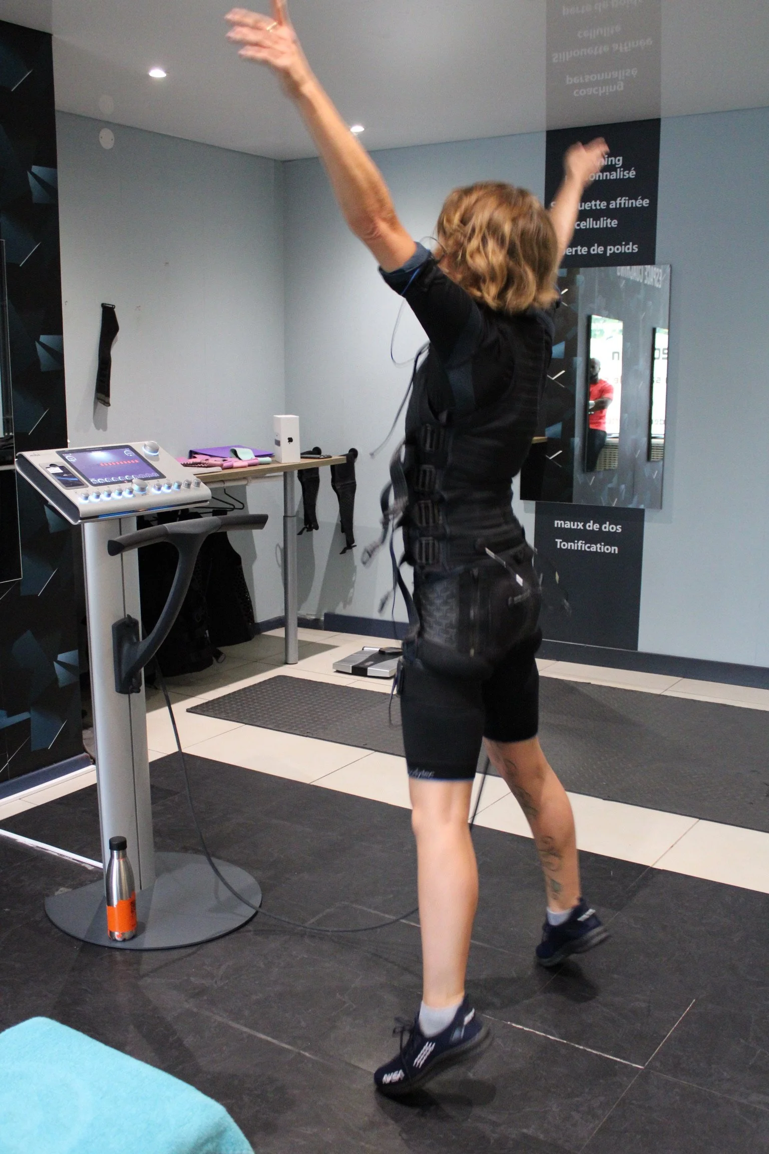 Femme en tenus d'EMS SOSTIM dans une salle de fitness ou de rééducation.