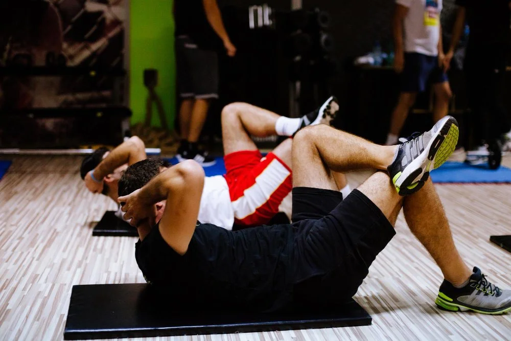 Deux hommes faisant des exercices abdominaux au sol dans une salle de sport.