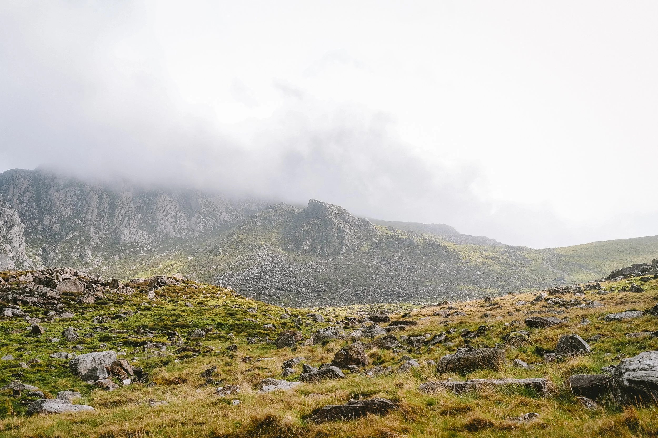 Mountain landscape with rocky slopes, green grass, and a cloudy sky.