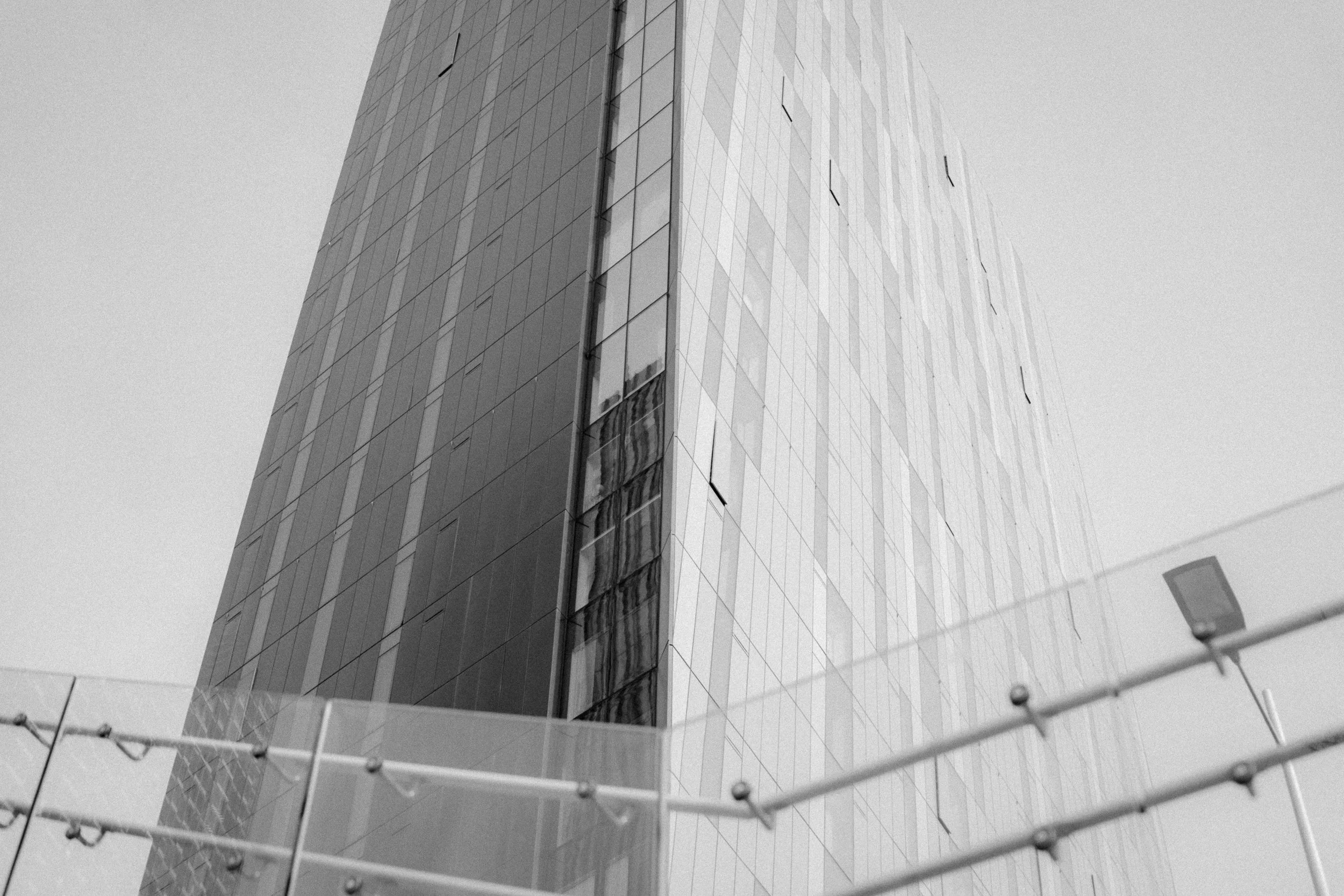 A tall modern building with reflective glass windows, viewed from a low angle, with part of a chain-link fence in the foreground.