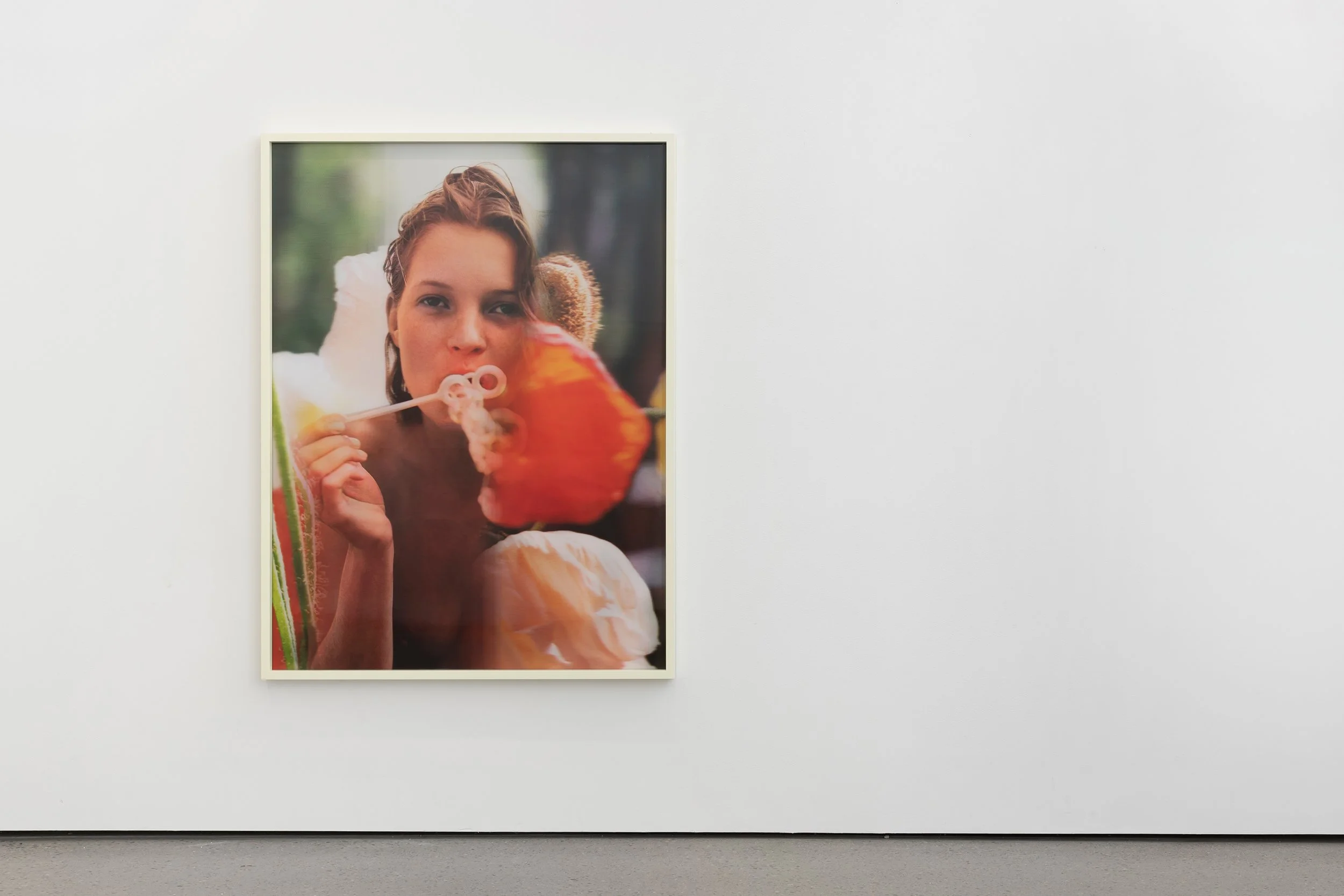 Color photograph of a young woman blowing bubbles with a bubble wand, shot outdoors with greenery blurred in the background.