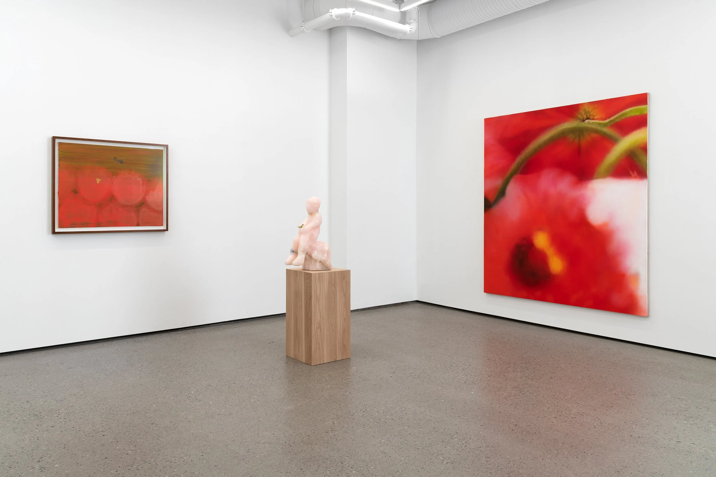 An art gallery with white walls displaying two framed paintings of red flowers and a pink sculpture on a wooden pedestal.